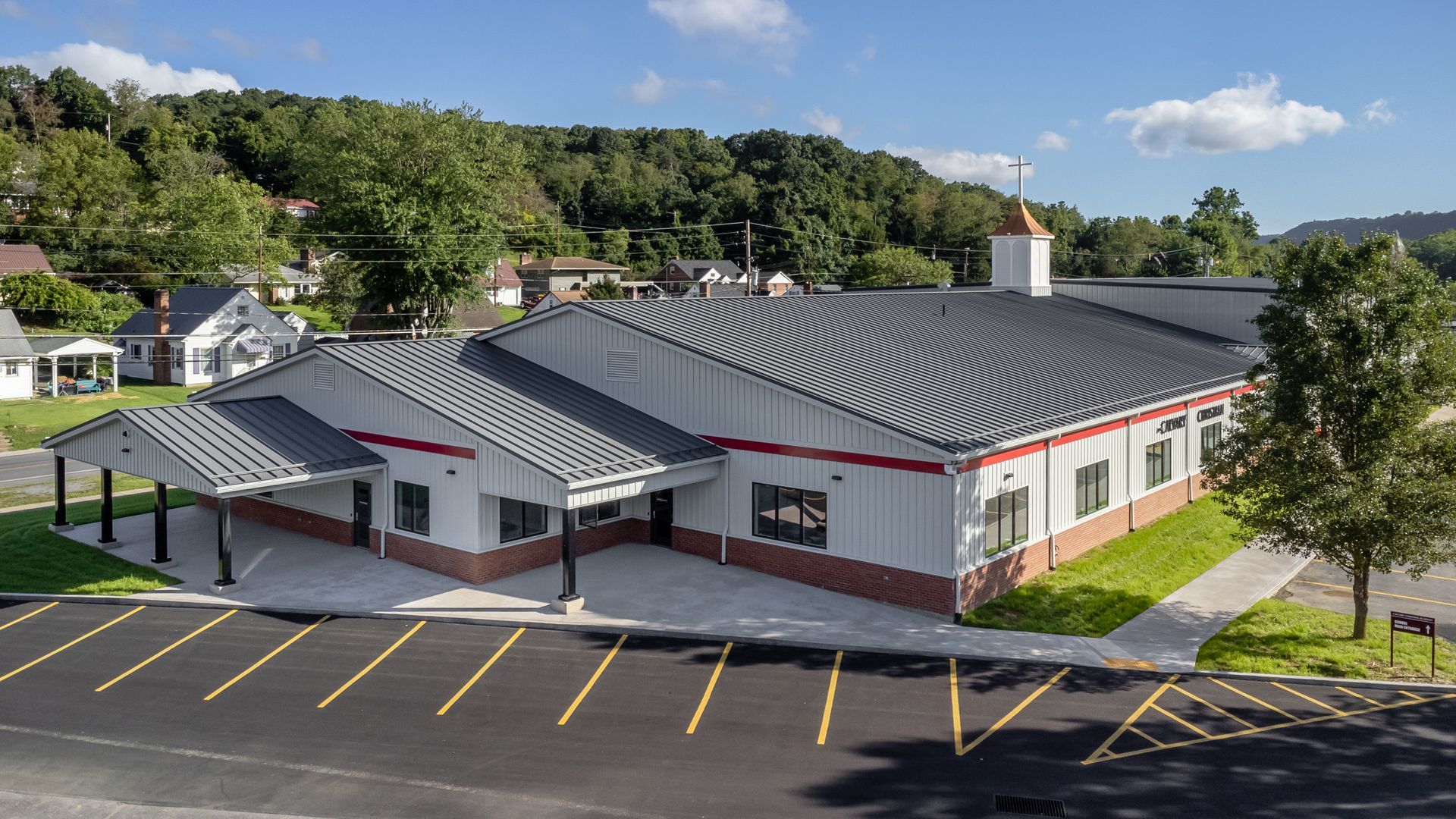 Exterior view of a one-story building with red trim and a gray metal roof in a parking lot.