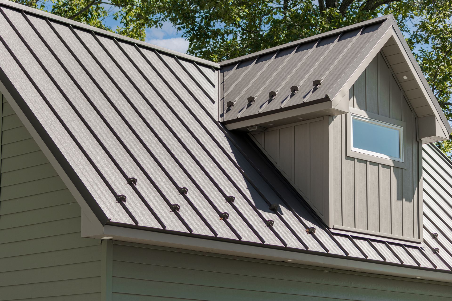 Metal roof on a light-colored house, with a small dormer and a window.