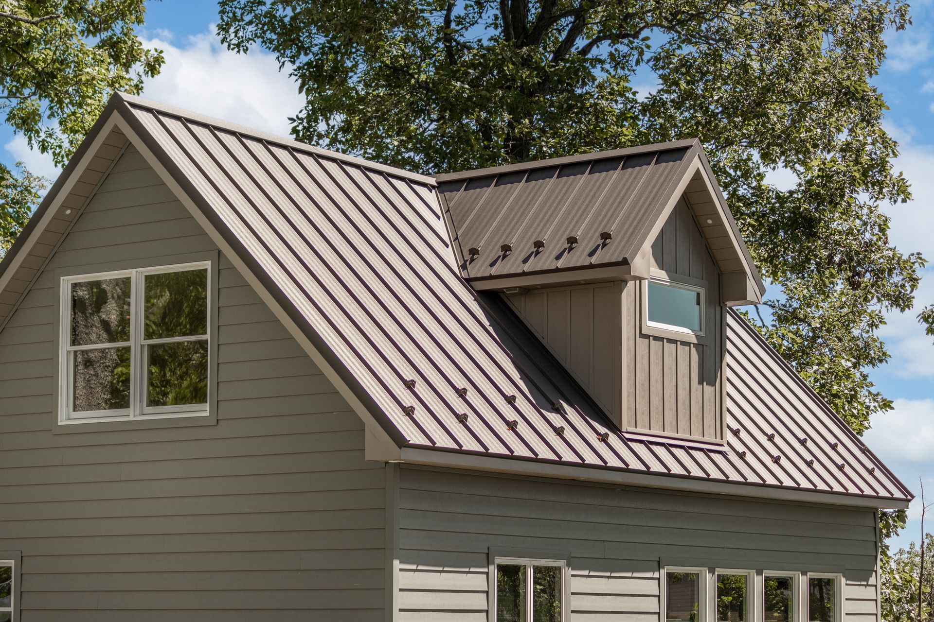 Gray house with a metal brown roof, dormer, and multiple windows.