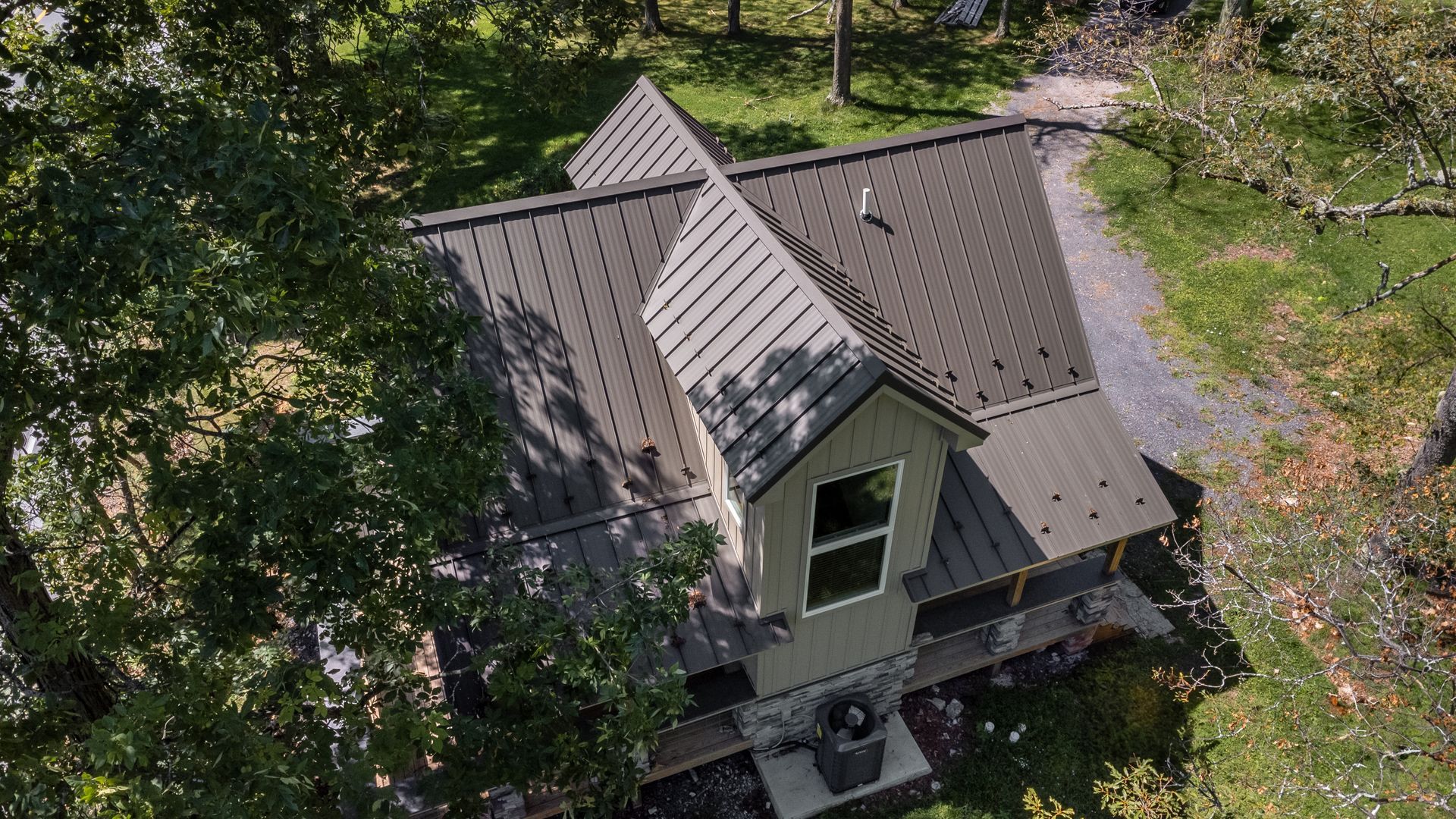Overhead view of a green cabin with a dark gray roof, surrounded by trees and green grass.