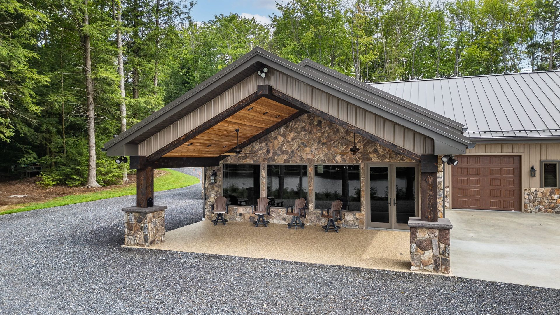 Stone and wood covered porch with seating, next to a garage, trees in the background.