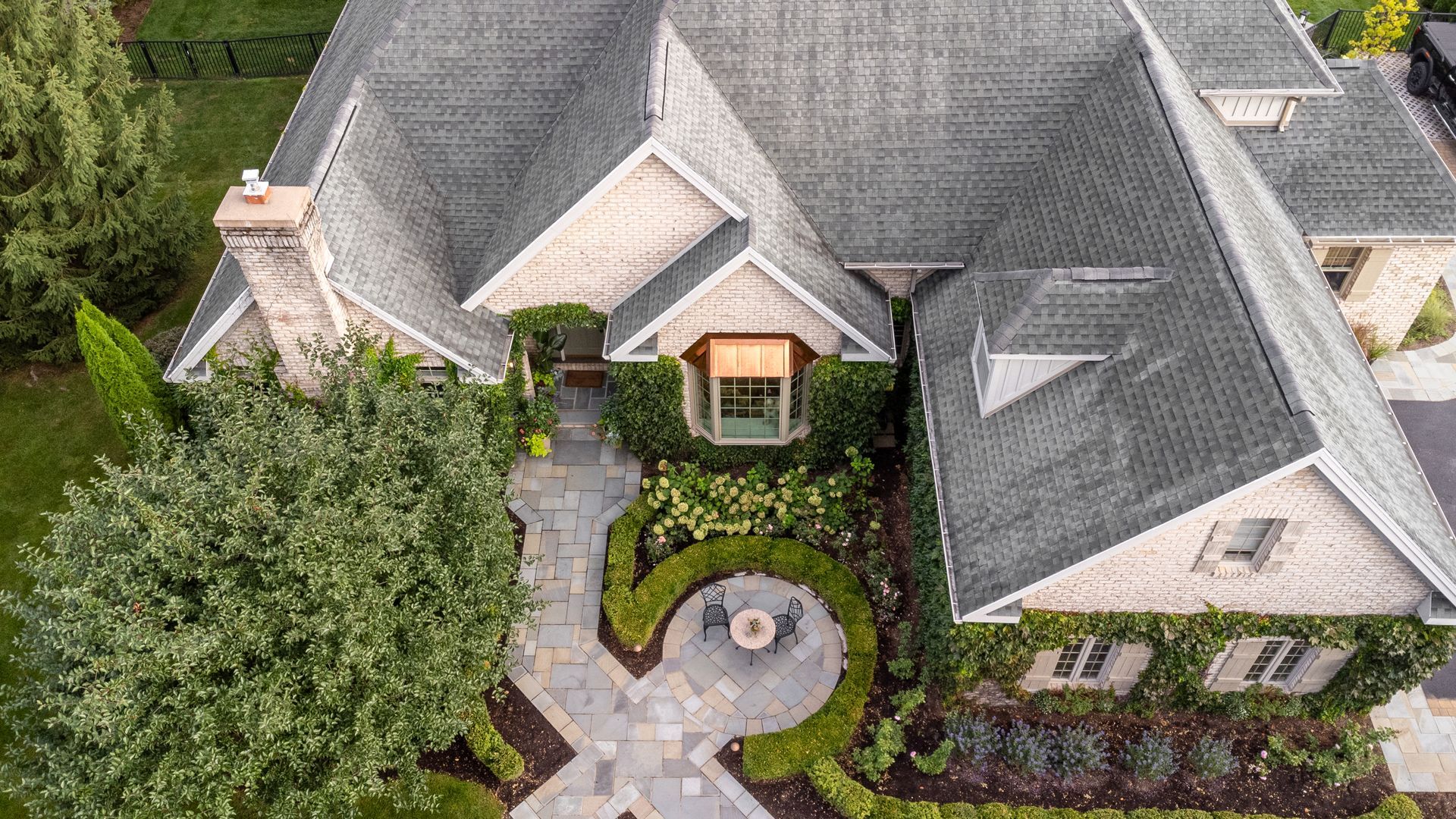 Overhead view of a luxurious stone house with gray roof, manicured garden, and a winding stone pathway.