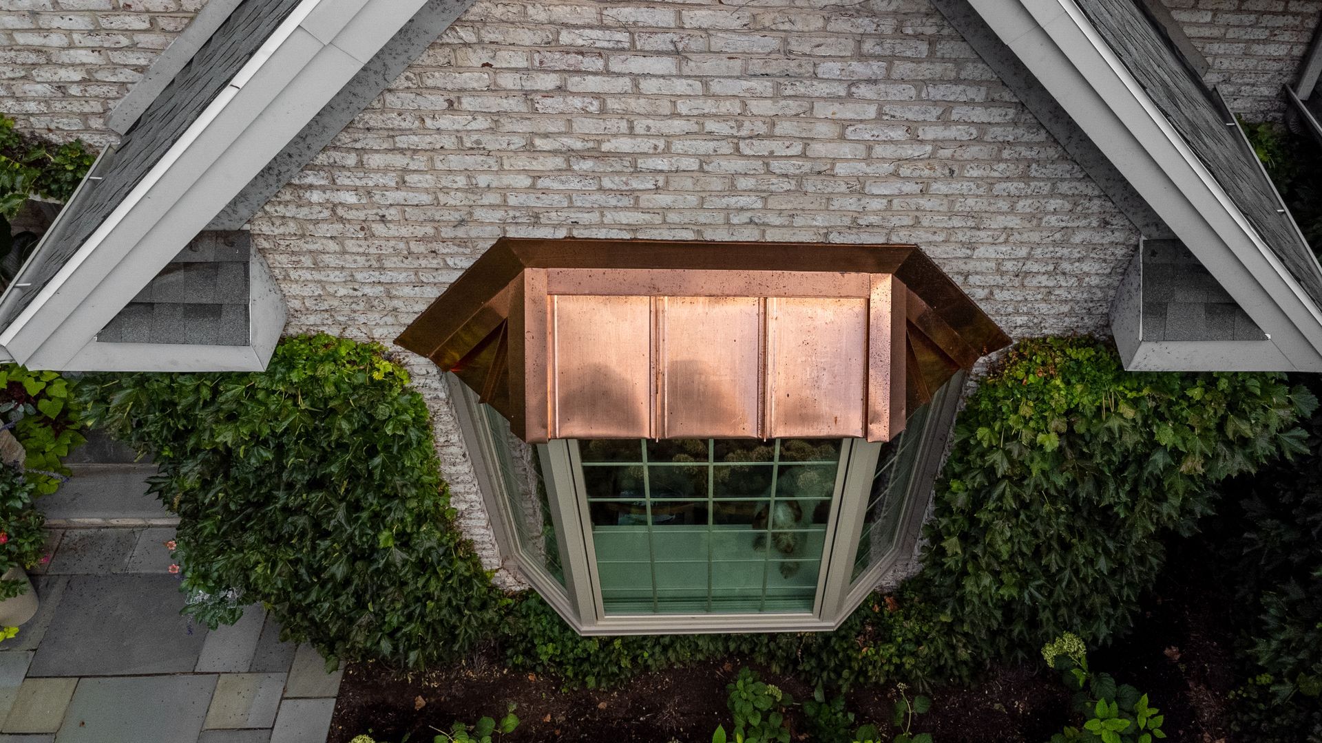 Copper-roofed window, surrounded by climbing ivy on a brick wall.