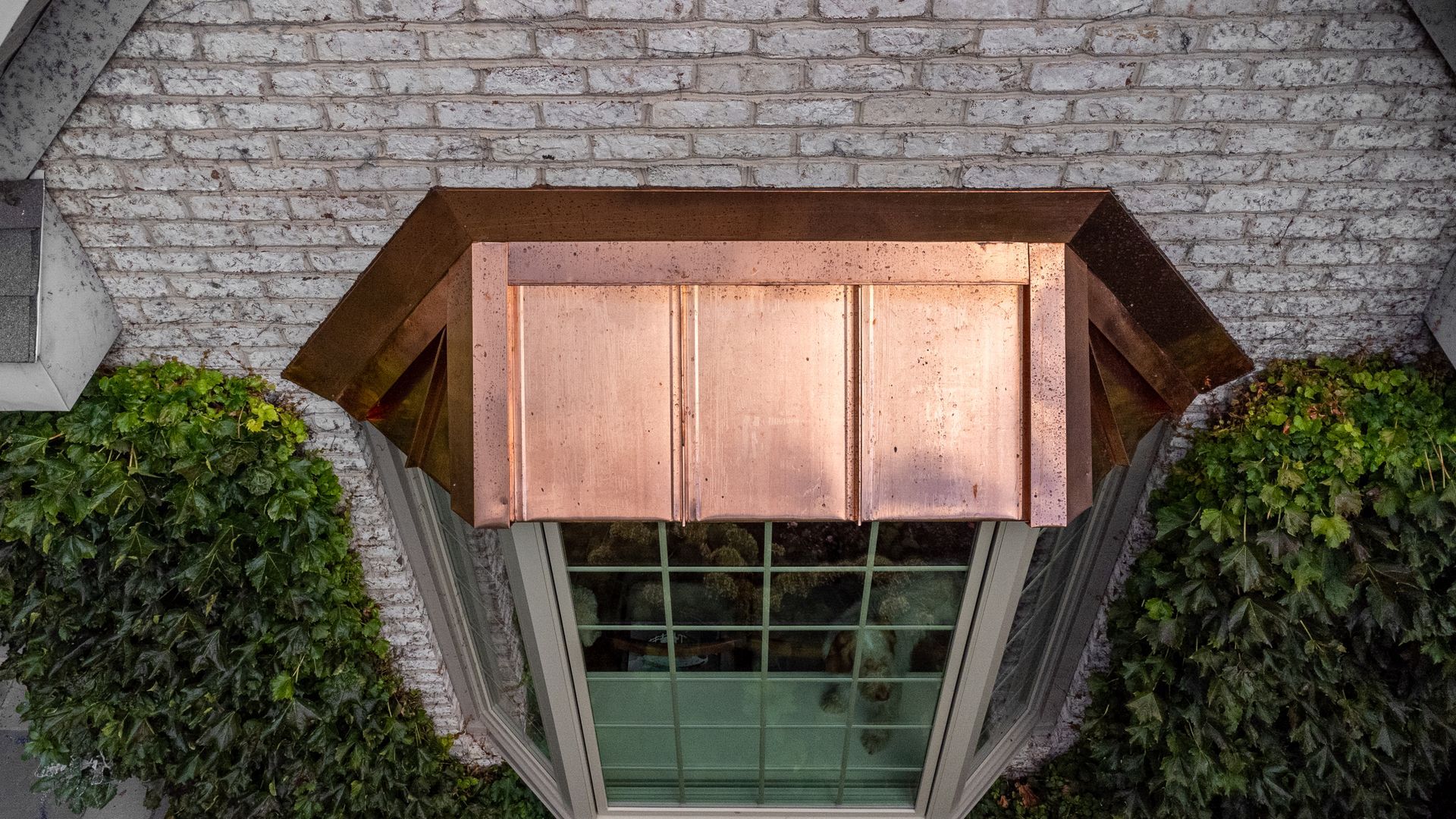 Copper-paneled box above a window, framed by brick and ivy-covered walls.