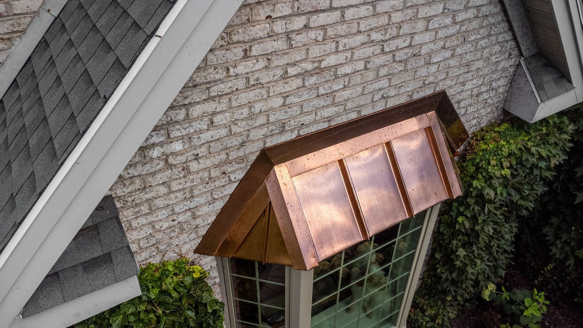 Copper-roofed window structure on a building with brick siding and dark shingle roof.