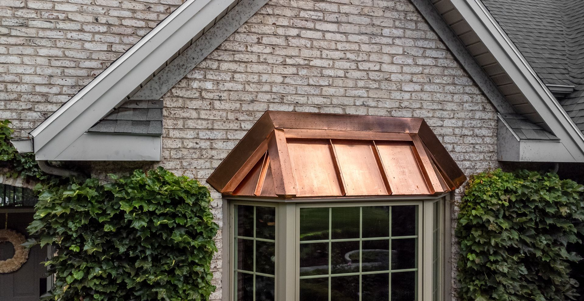 Copper bay window roof on a brick house, with green ivy on the sides.