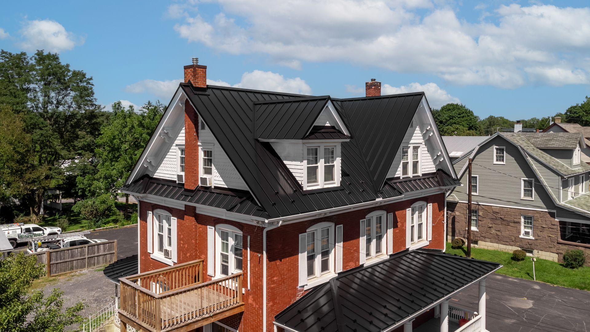 Red brick house with black metal roof and white trim, on a sunny day.