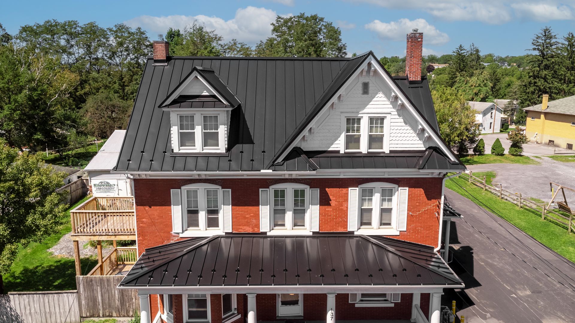 Red brick house with black roof, white trim, two dormers, and a porch.