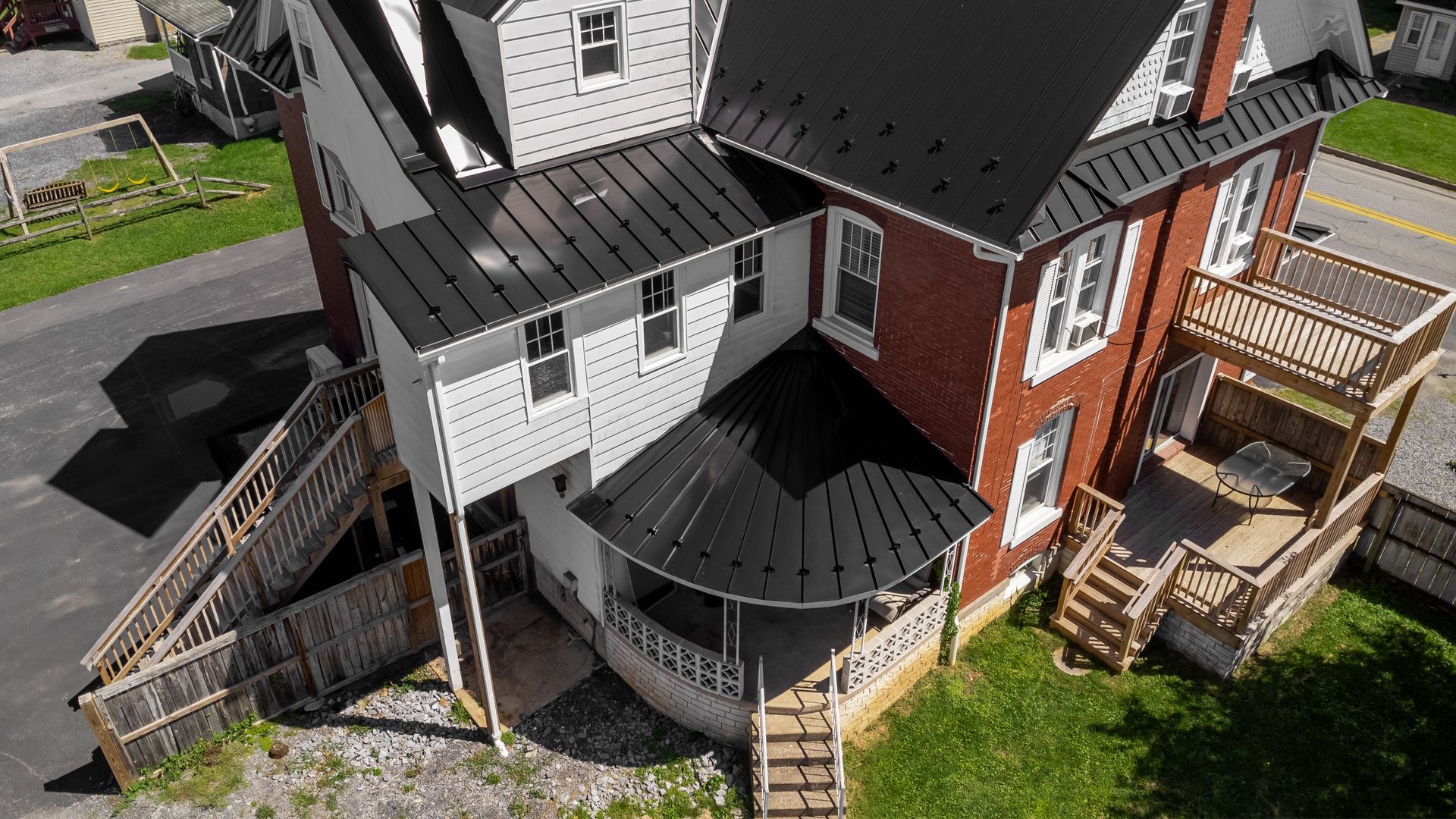 Two-story house with black roof, red brick and gray siding, wooden deck, and porch.