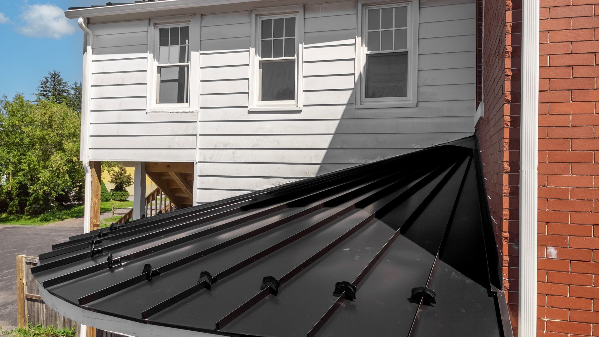 Black metal roof against a white clapboard building with three windows and a red brick wall on the right.