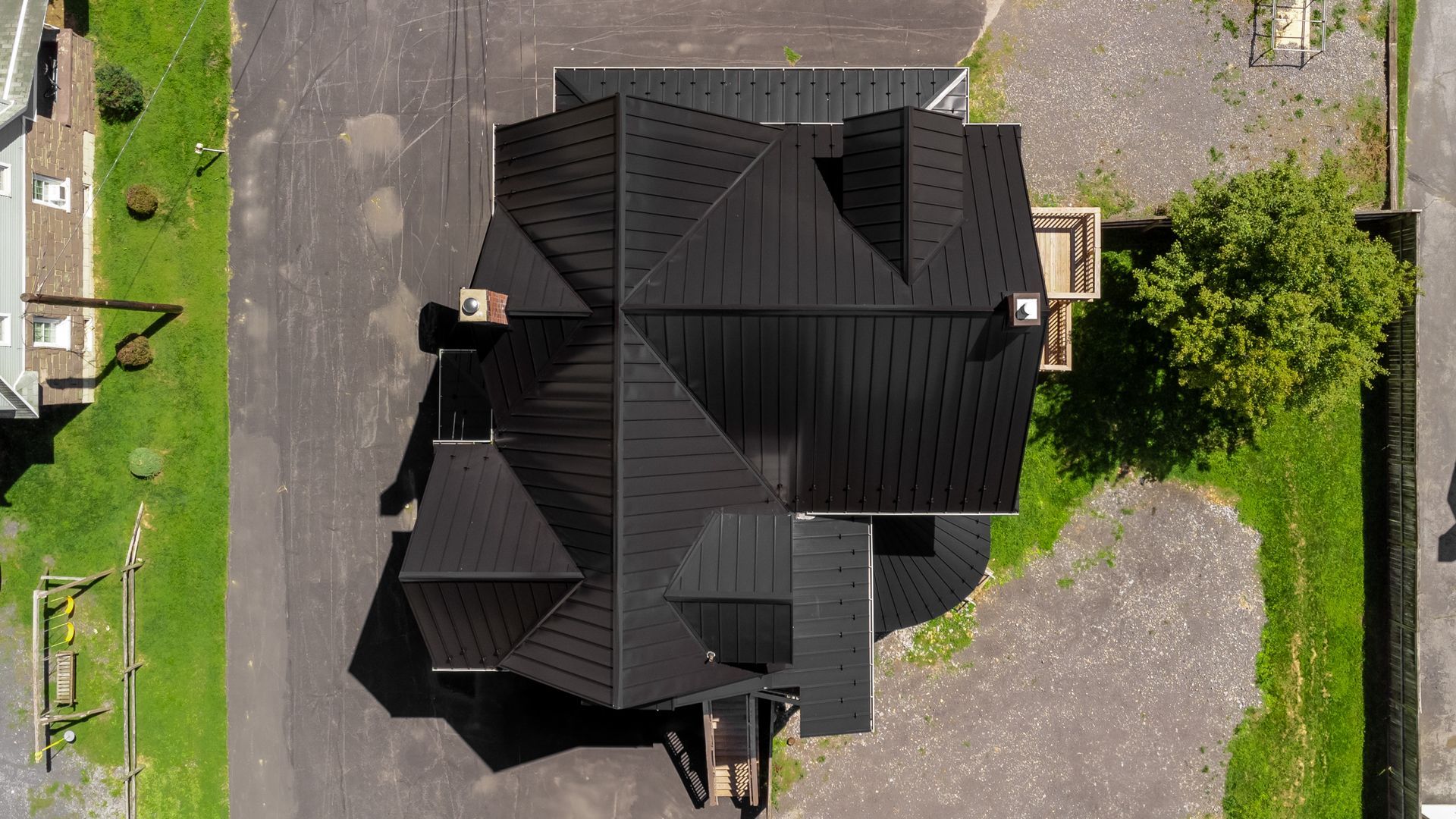 Overhead view of a black-roofed house with a complex shape surrounded by asphalt and grass.