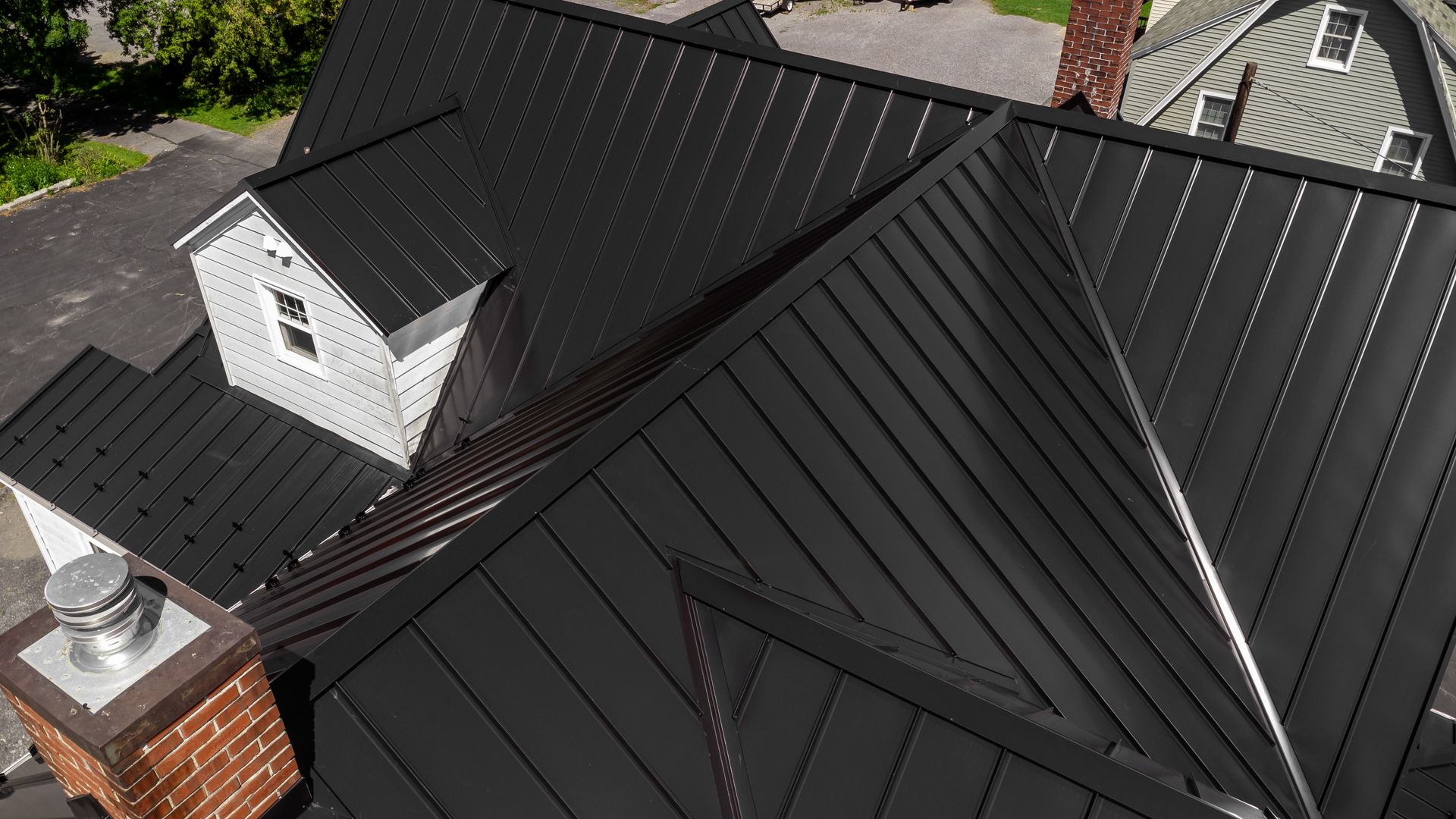 Black metal roof on a house with a brick chimney and a dormer.