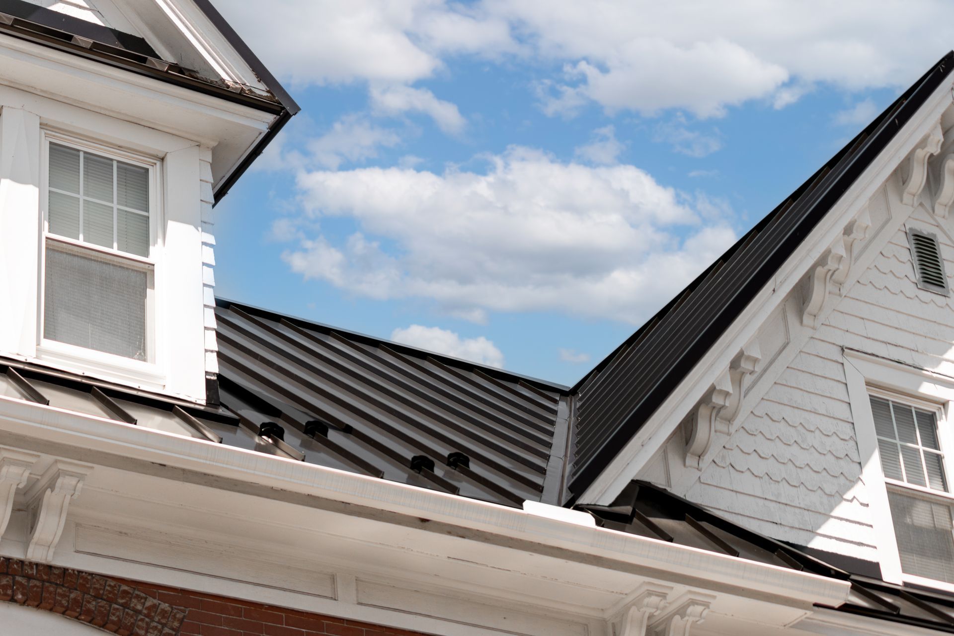 White house with black metal roof against a blue sky with clouds.