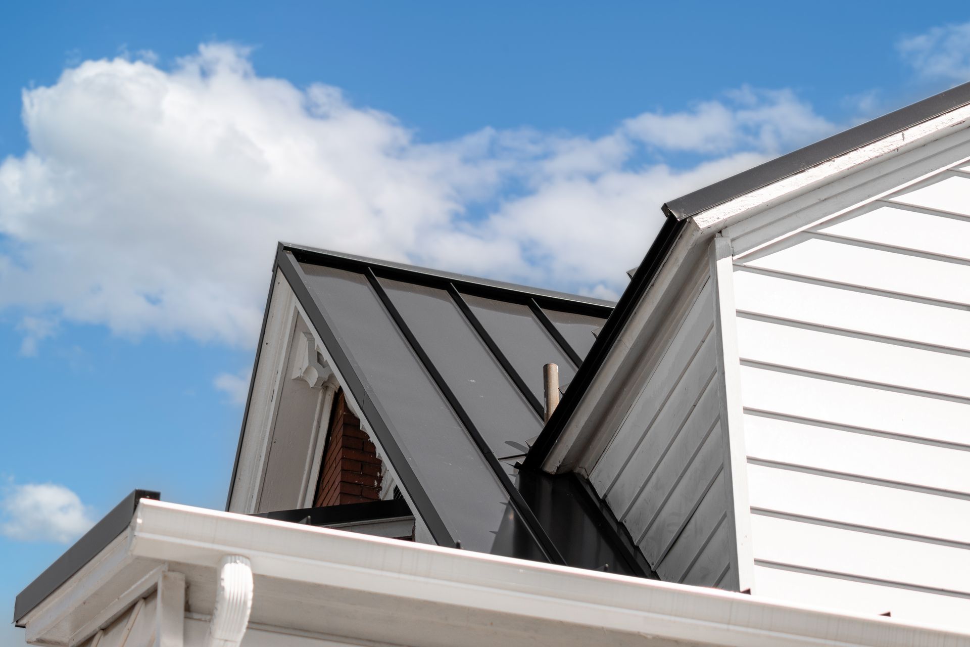 White house with a dark gray metal roof against a blue sky with white clouds.