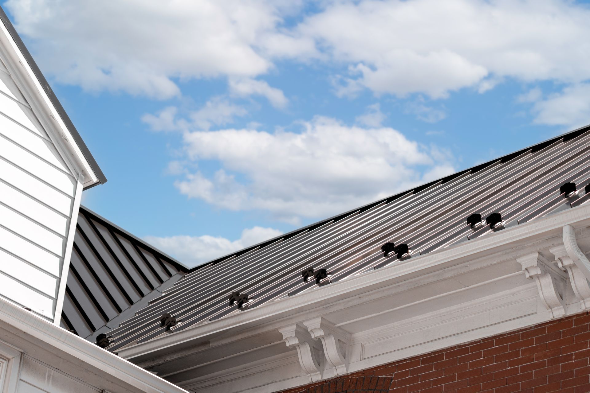 Metal roof with black bird deterrents, white siding, and a blue sky with clouds.