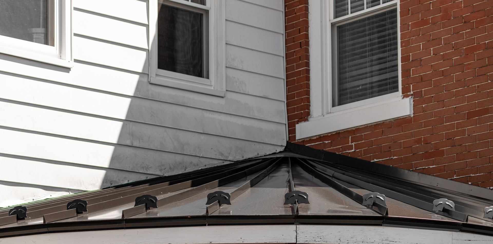 Metal roof meets white siding and brick wall with windows.