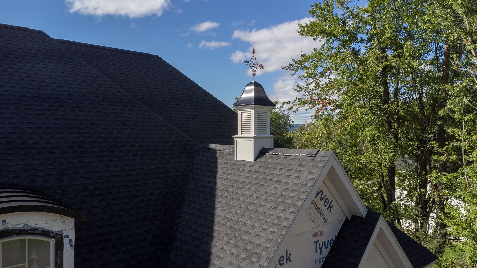 Dark roof of a house with a small steeple, and a weather vane on top.