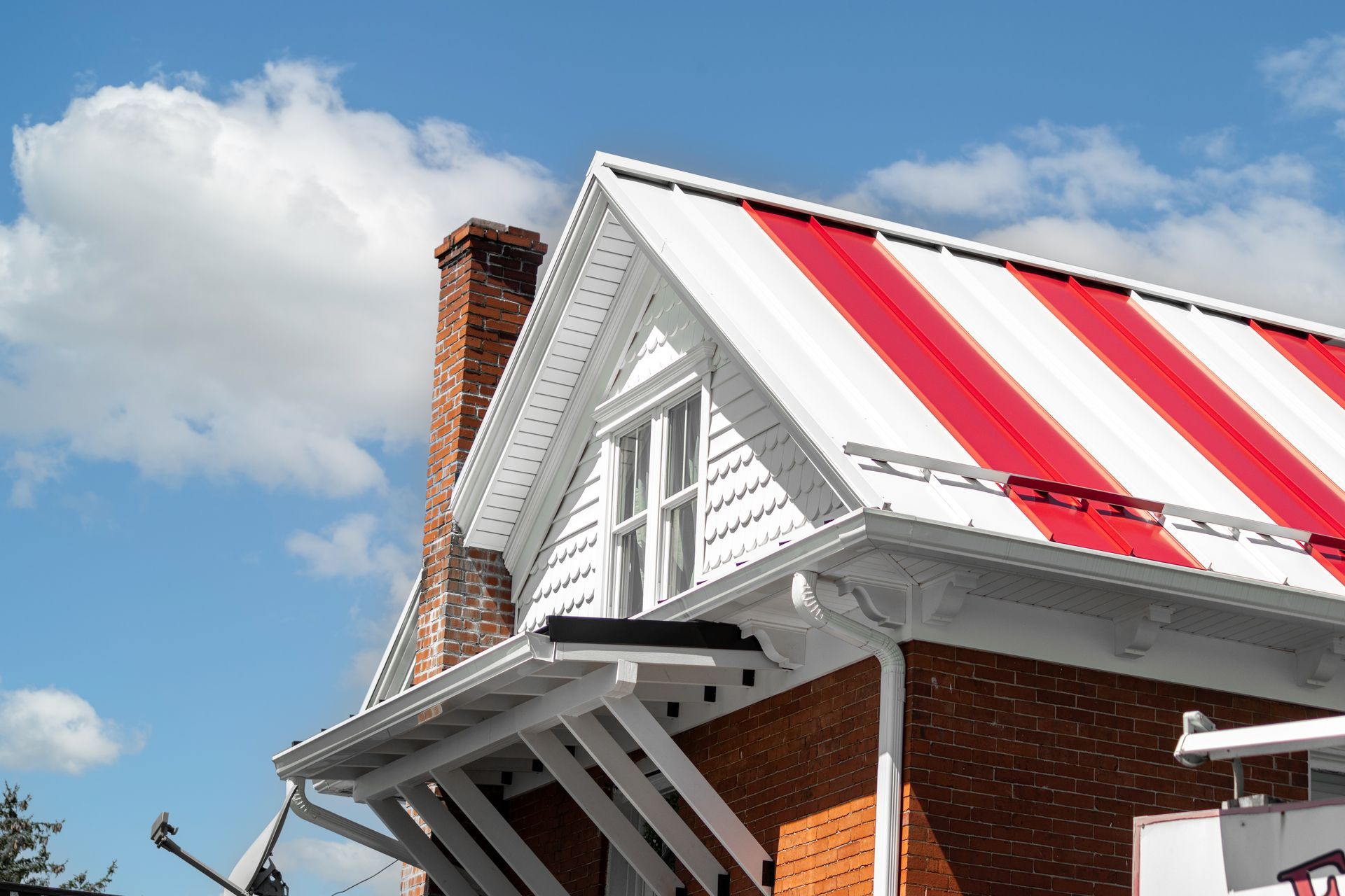 Brick building with a red and white striped metal roof, chimney, and a bright blue sky.