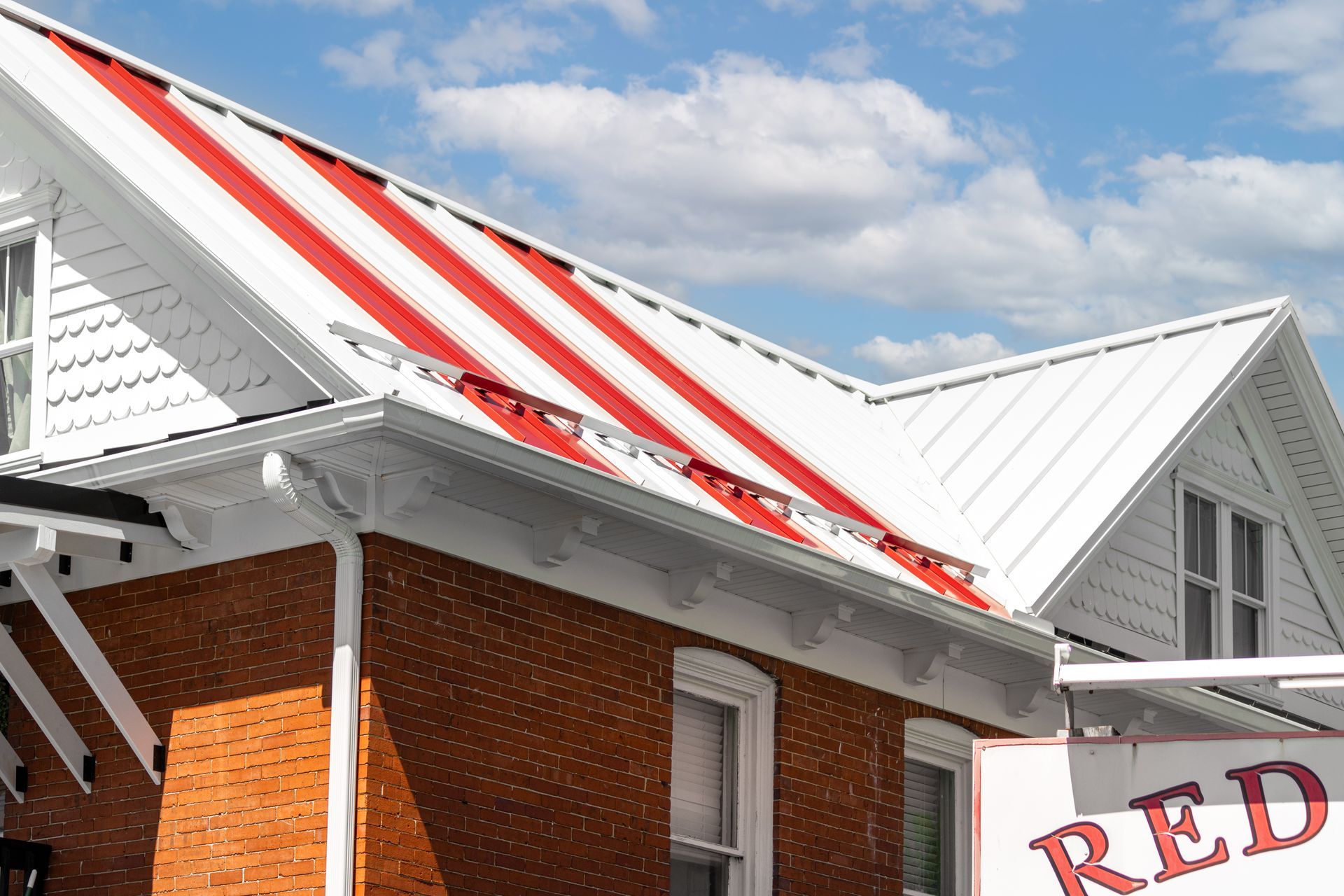 Brick building with white roof, alternating red stripes. Blue sky with clouds in background.