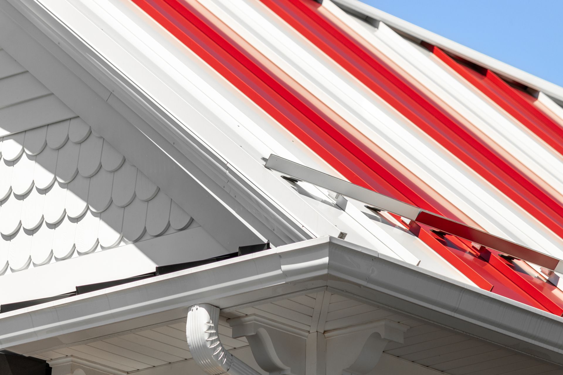 Red and white striped metal roof on a white house with white trim, a gutter and decorative shingles.