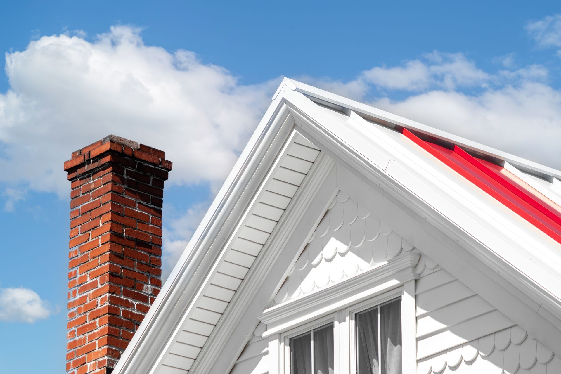 Brick chimney next to a white house with a red roof accent, set against a blue sky with clouds.