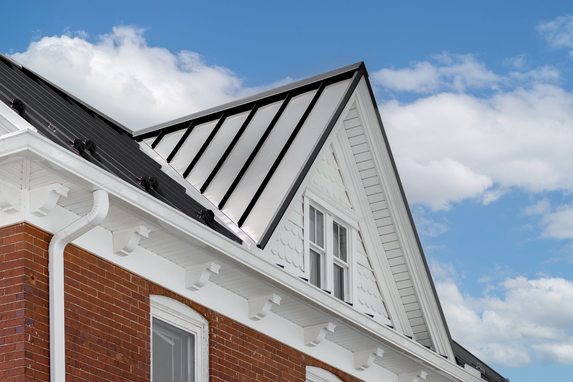 Brick building with white trim, a black metal roof, and blue sky.