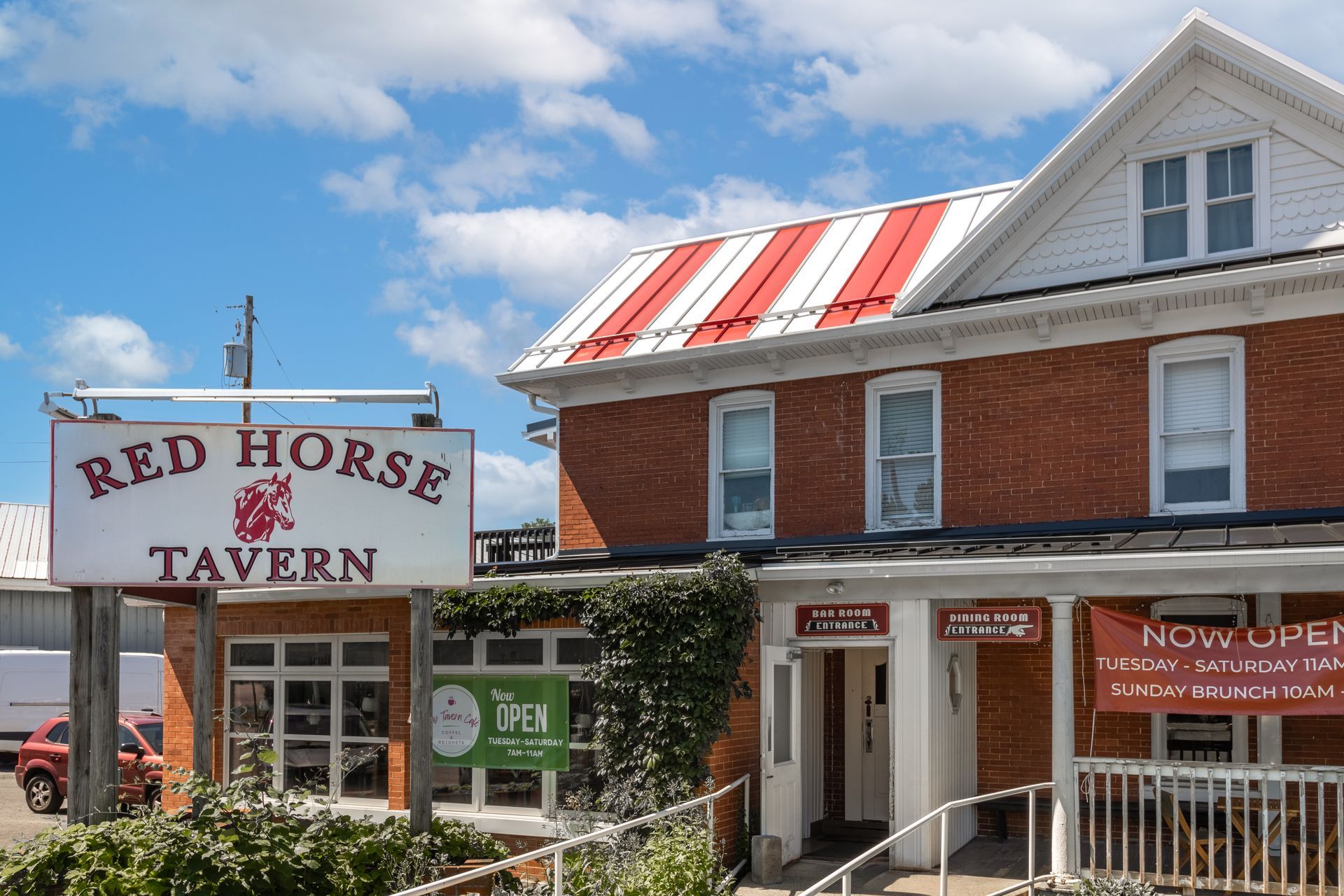 Red Horse Tavern with sign, brick building, red and white striped roof, under a blue sky.