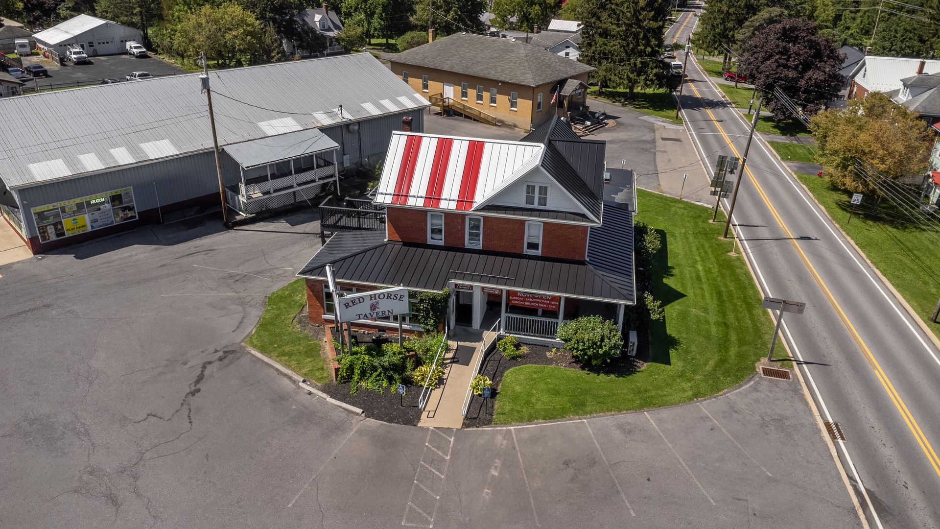 Aerial view of a brick building with a red and white striped roof, surrounded by pavement and a road.