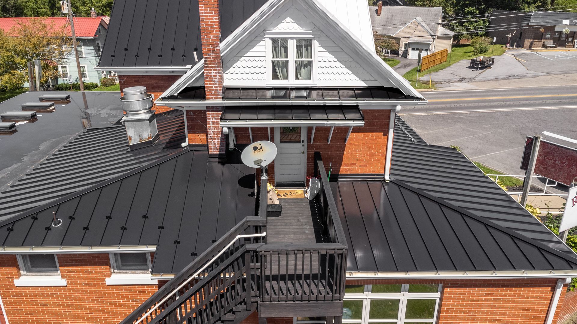 A black metal roof on a brick building with an outdoor deck and staircase; satellite dish on the roof.
