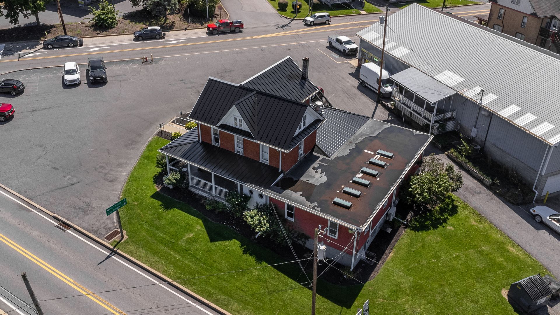 Aerial view of a red brick building with a black roof, adjacent to a large gray building and a street.