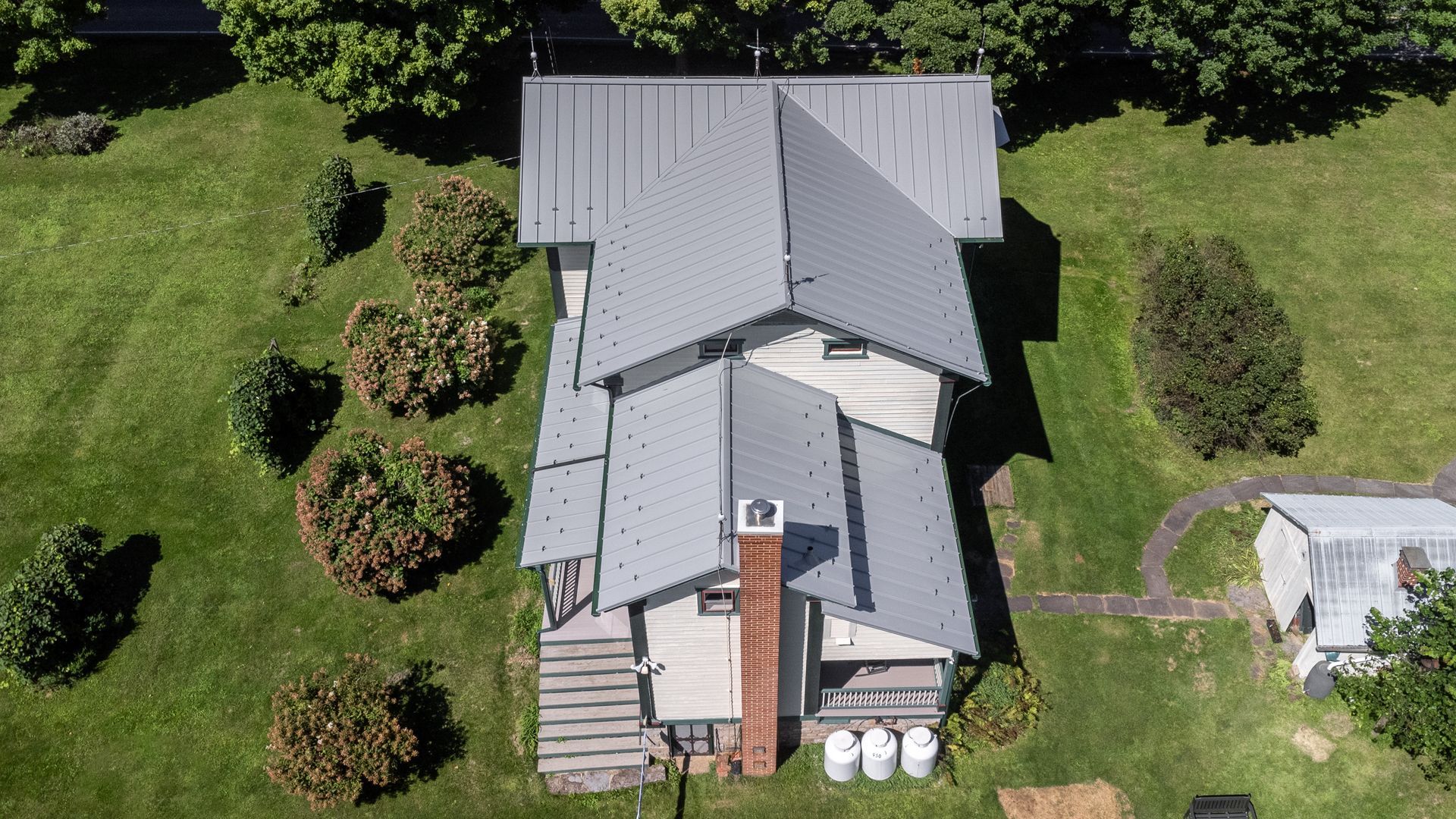 Aerial view of a house with a gray roof and a brick chimney, surrounded by green grass and shrubs.