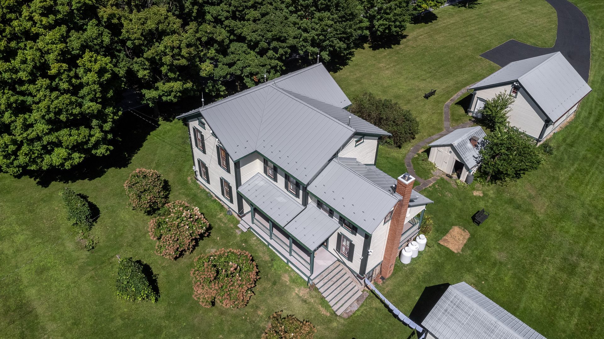Aerial view of a two-story house with a gray roof and several outbuildings on a green lawn.