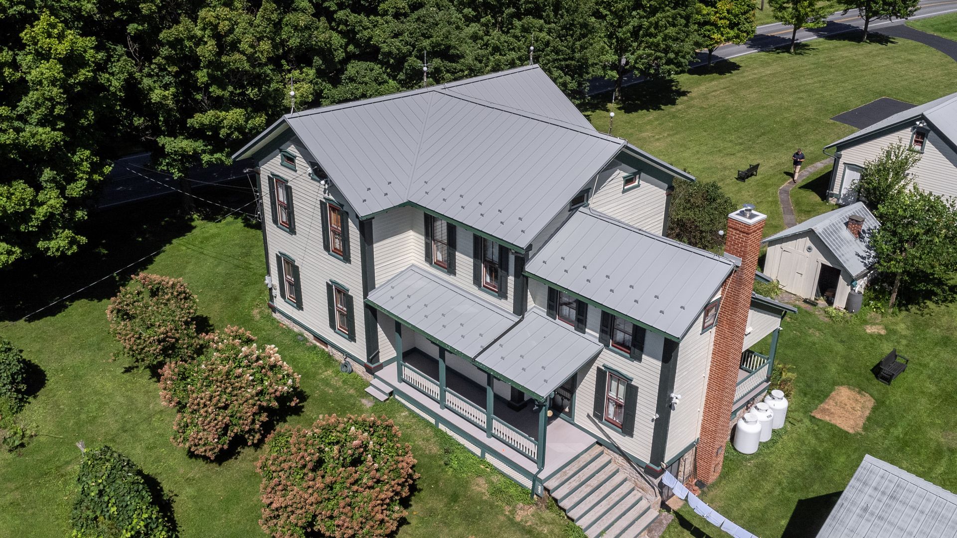 Two-story house with gray roof, green grass, tan walls, and black shutters.