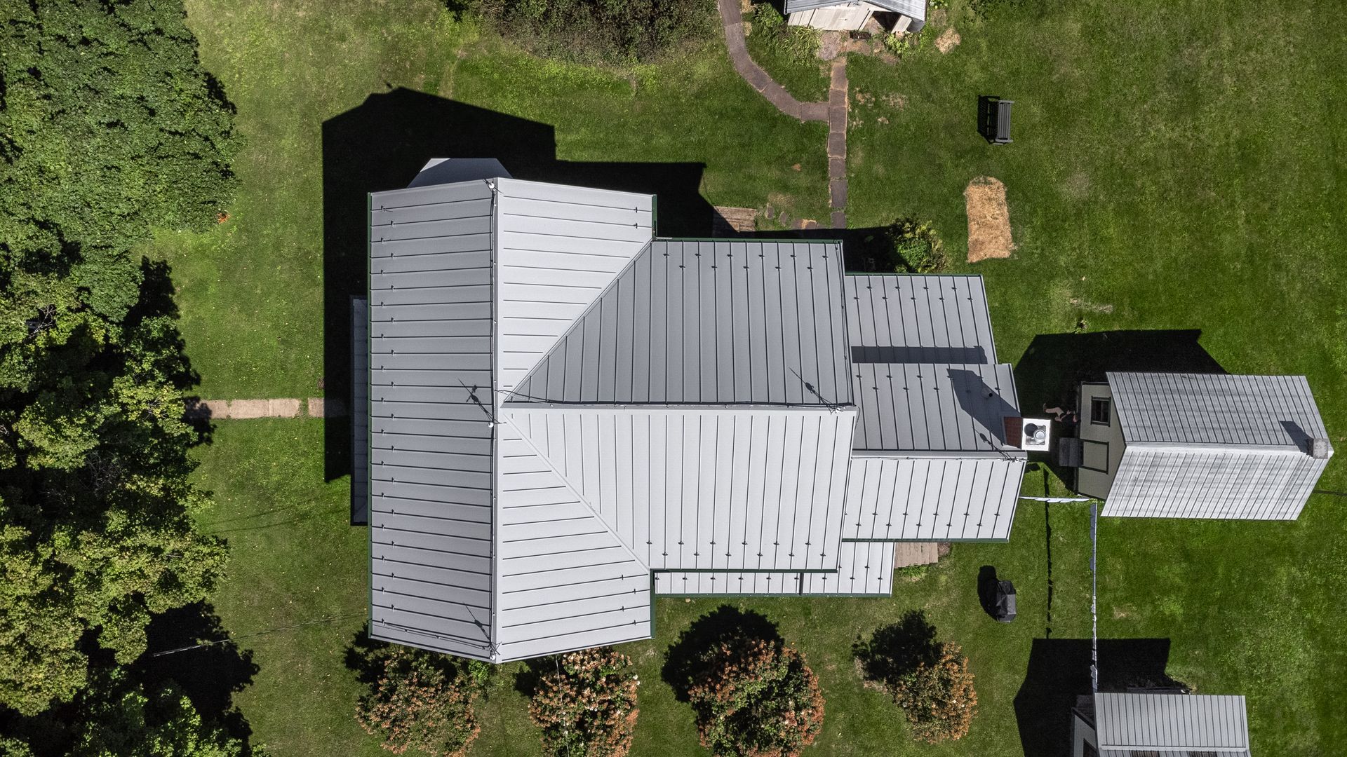 Overhead view of a gray-roofed building on a grassy lot, trees in the foreground and background.