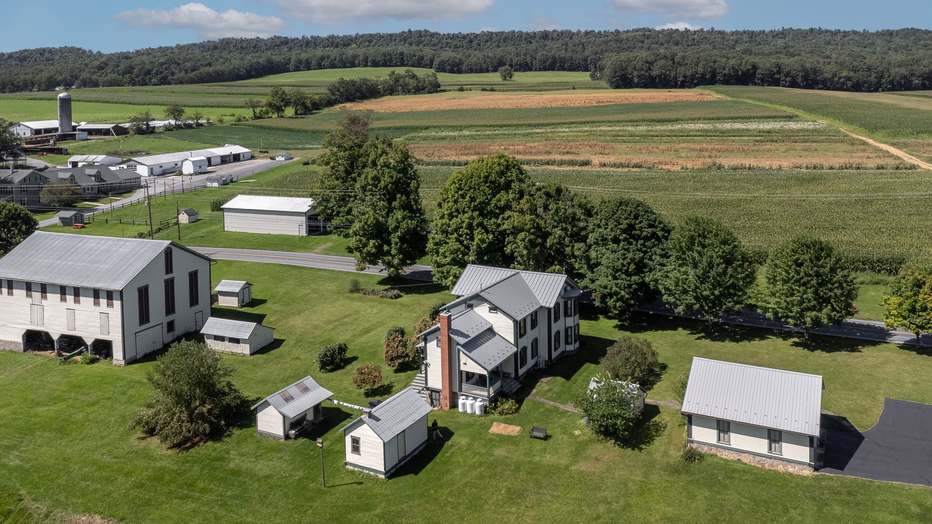 Farm with white buildings, green grass, and crops in the background on a sunny day.