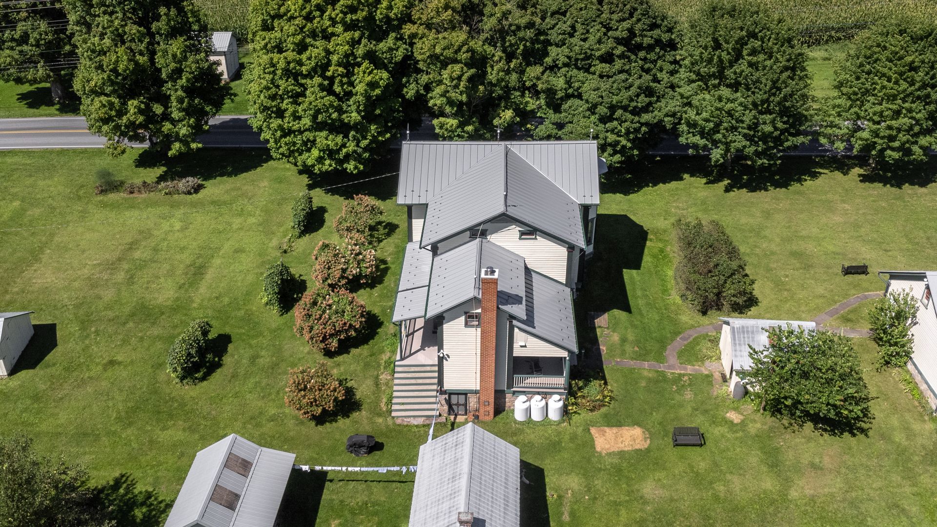 Aerial view of a gray-roofed house with a brick chimney on a green lawn, trees surround the property.