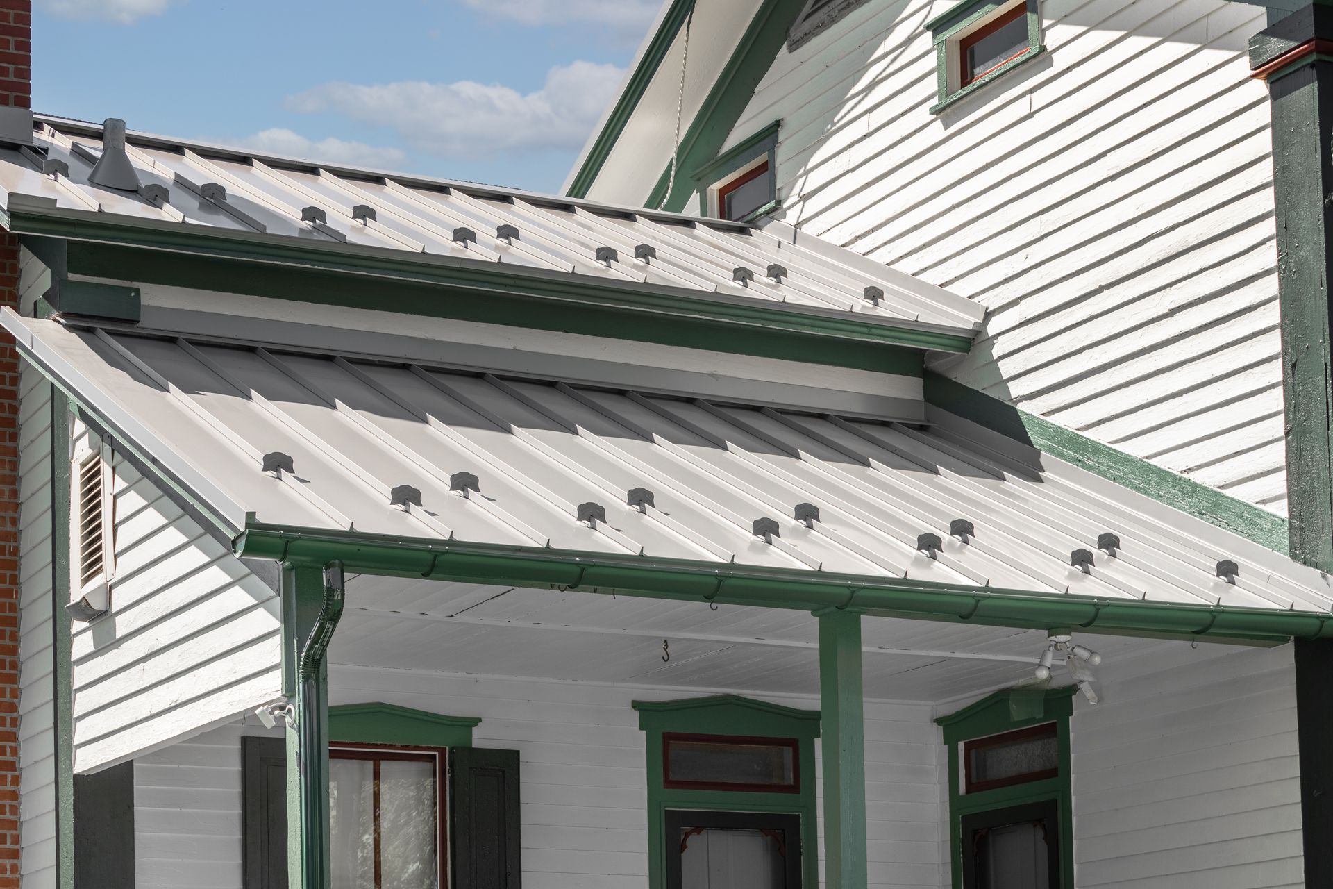 White house with gray metal roof and green trim.