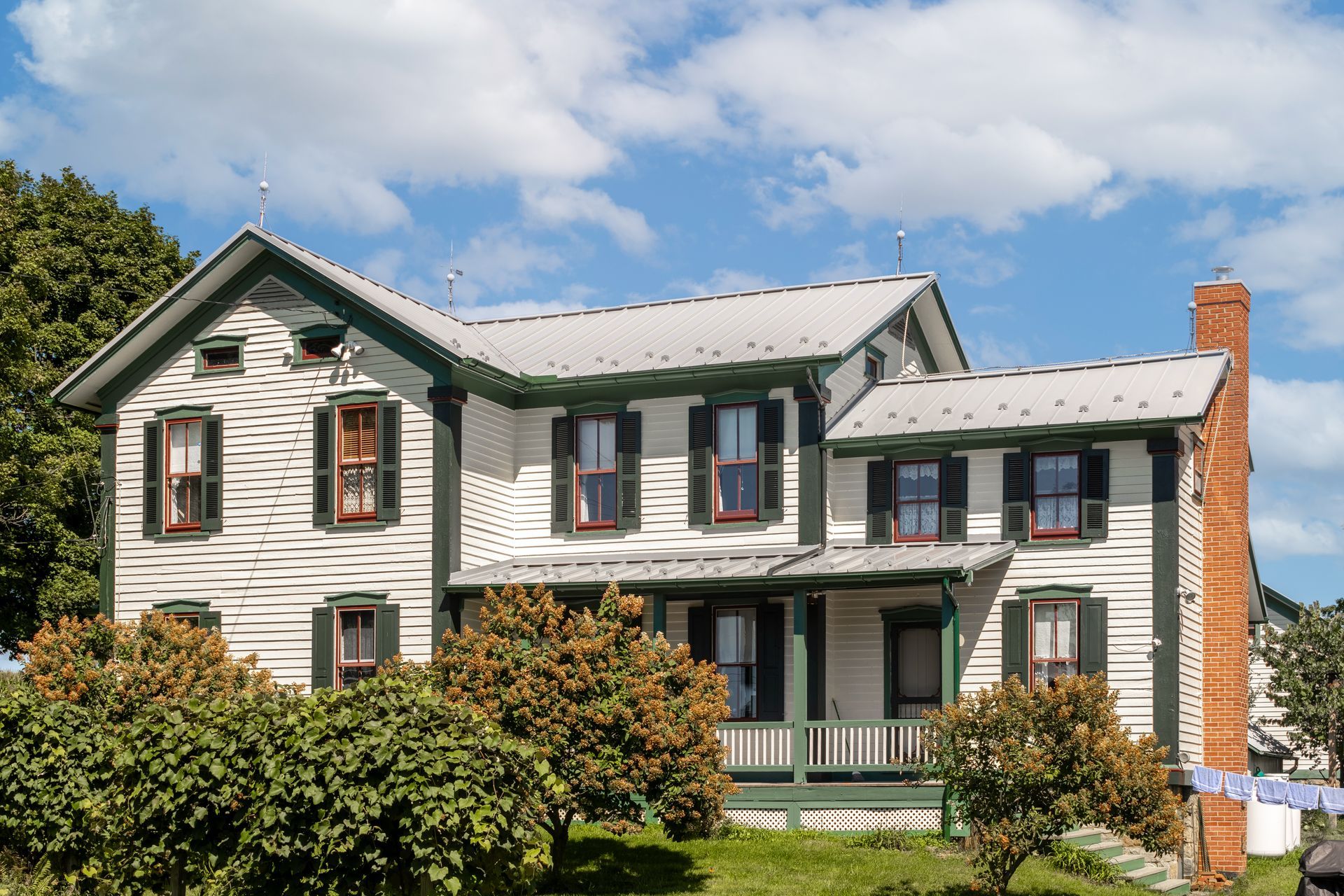 White house with green trim and shutters, red brick chimney, cloudy sky.