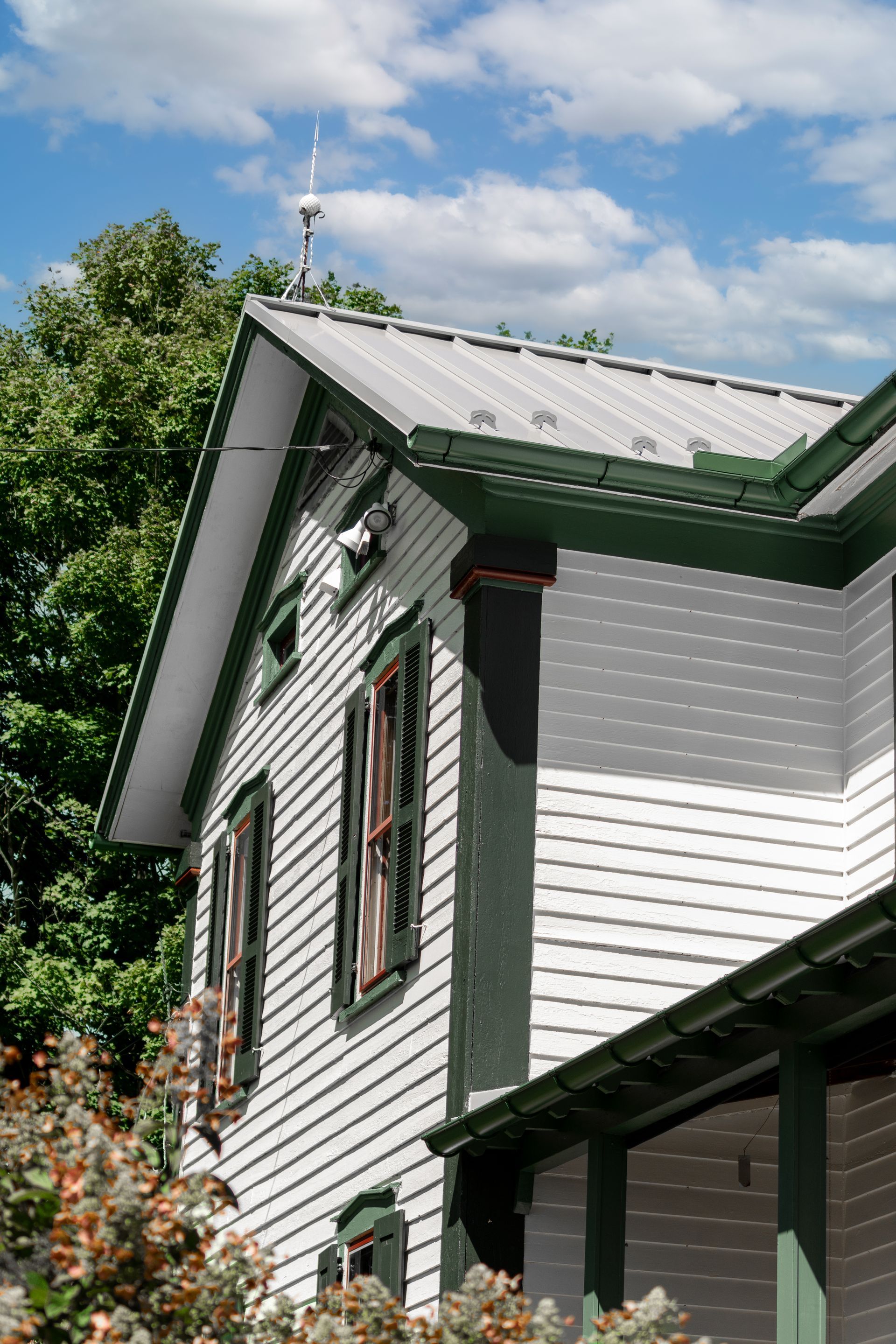 White house with green trim and metal roof against a blue sky.