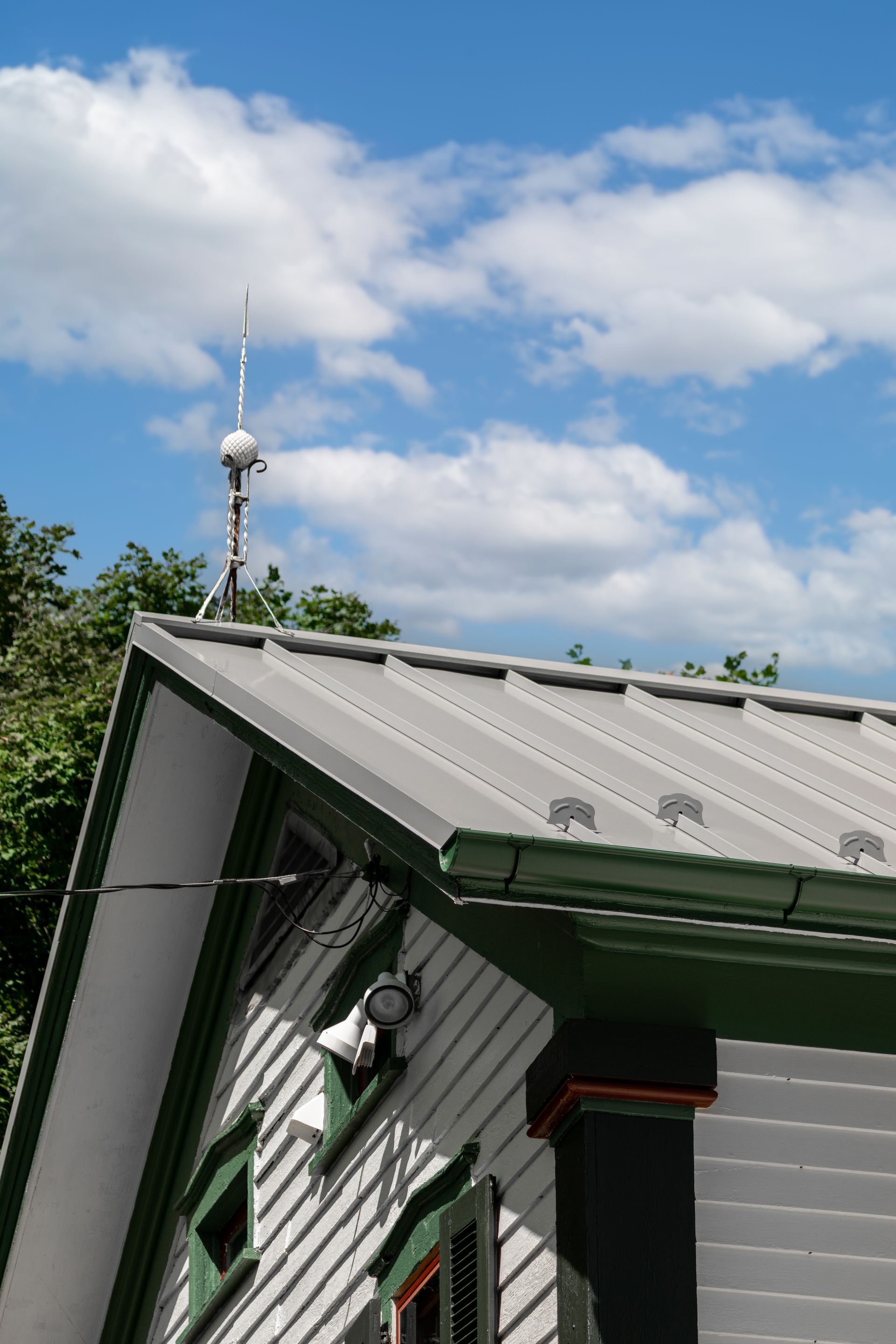White house with gray roof, green trim, and antenna against a cloudy blue sky.