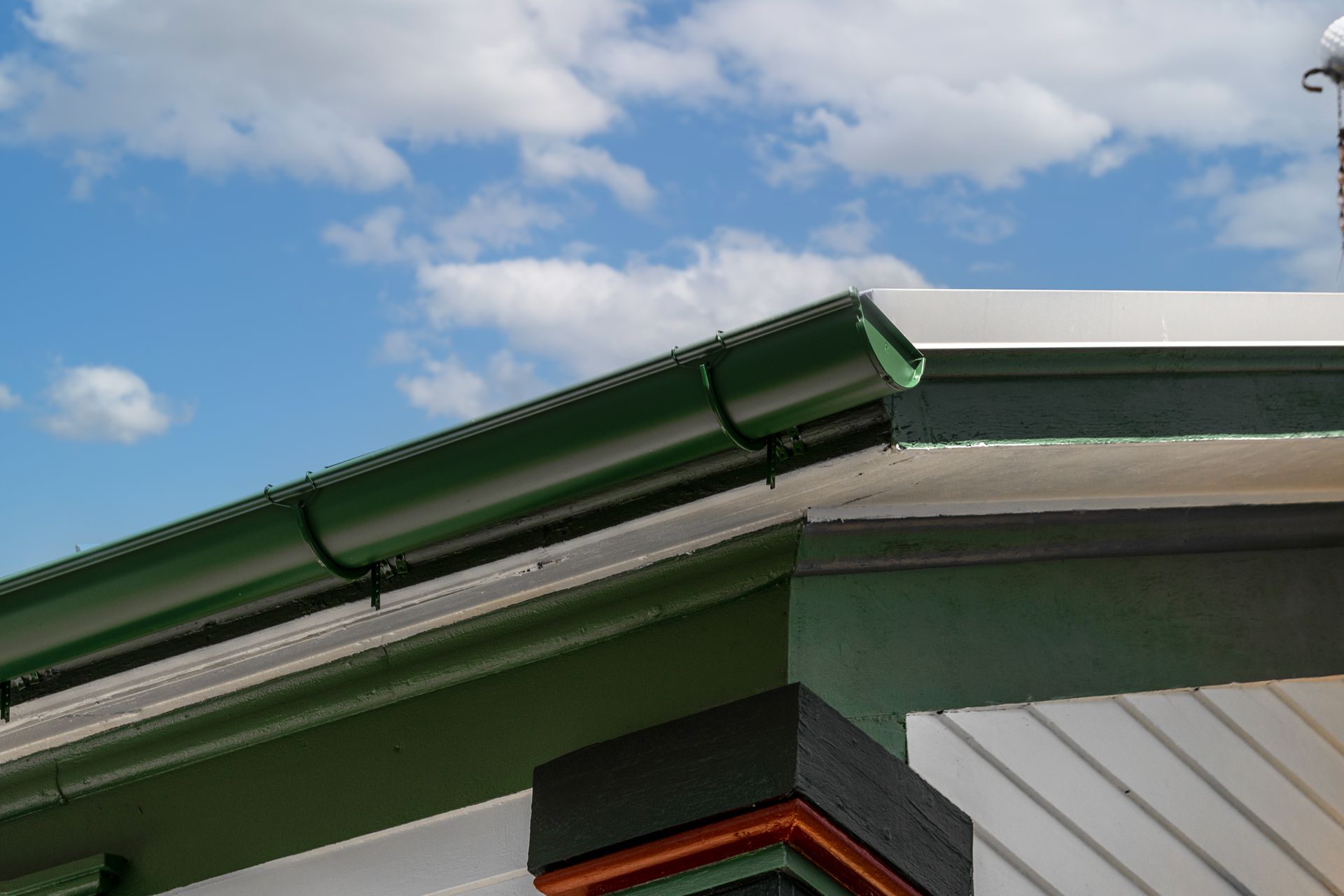 Green rain gutter on a building's roof, against a blue sky with fluffy white clouds.