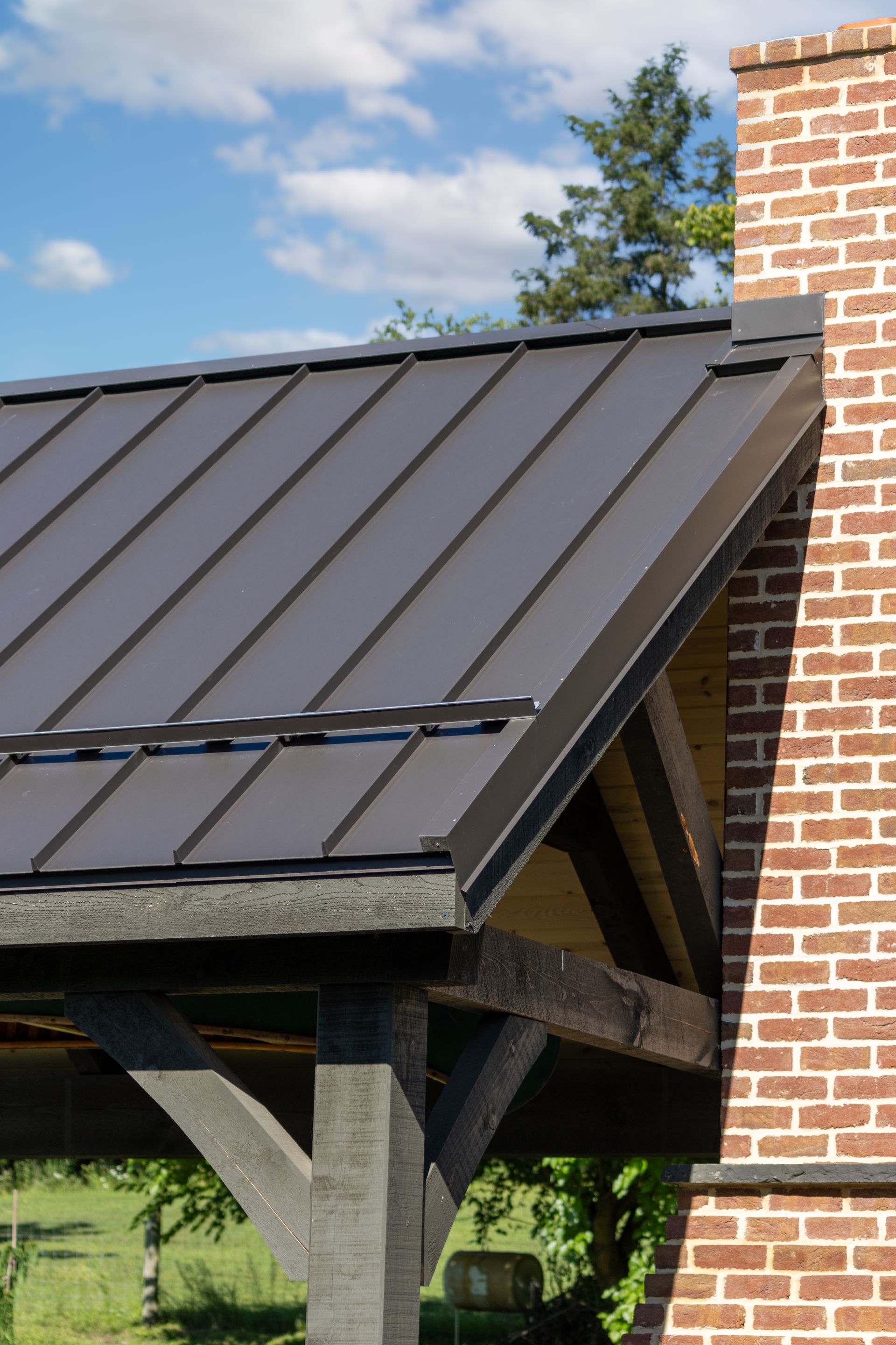 Brown metal roof and wooden beams, next to a red brick chimney, under a blue sky.