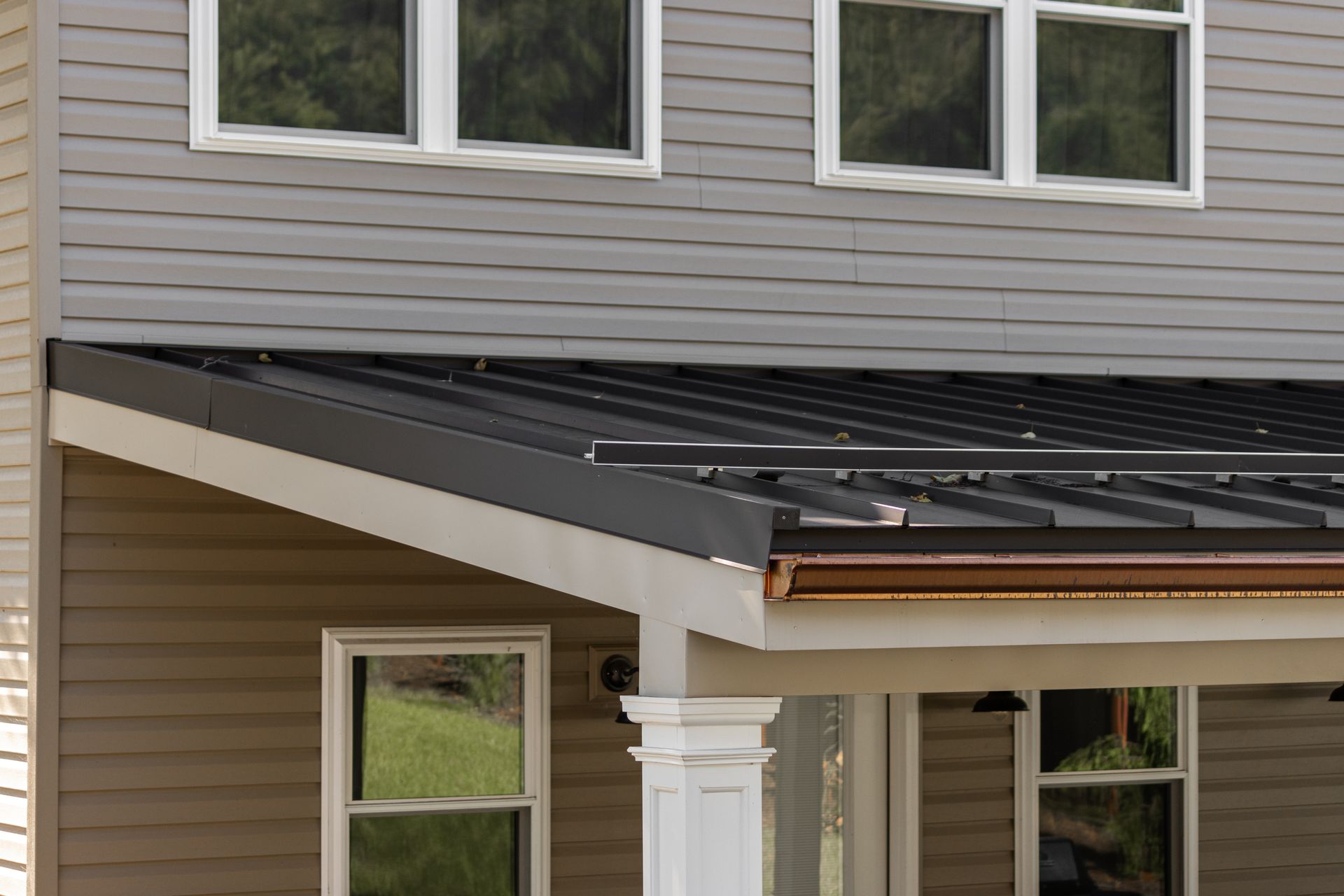 Gray and beige house with metal roof, white trim windows, and porch columns.