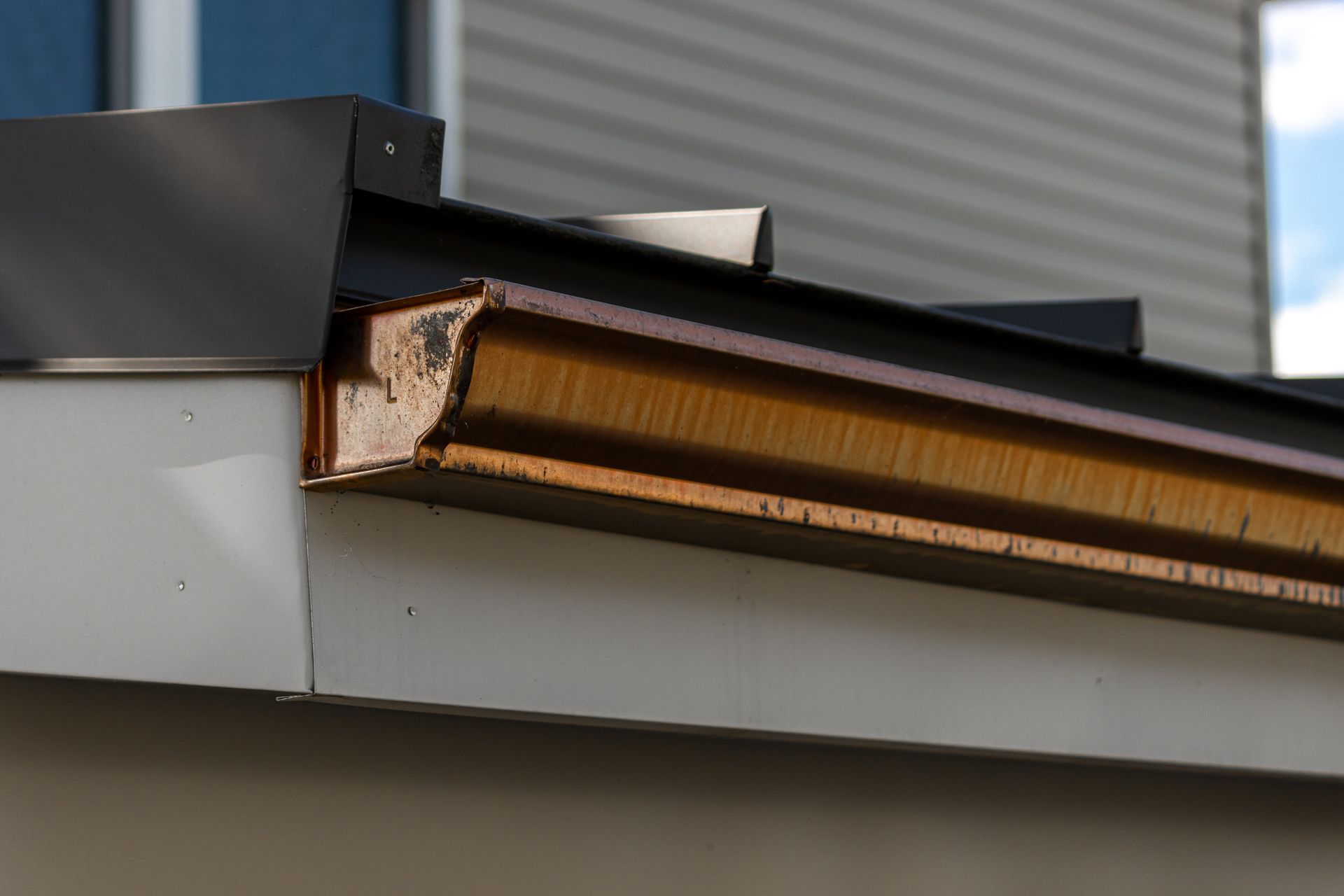 Close-up of a building's rain gutter, showing copper and metal materials, with light brown and grey colors.