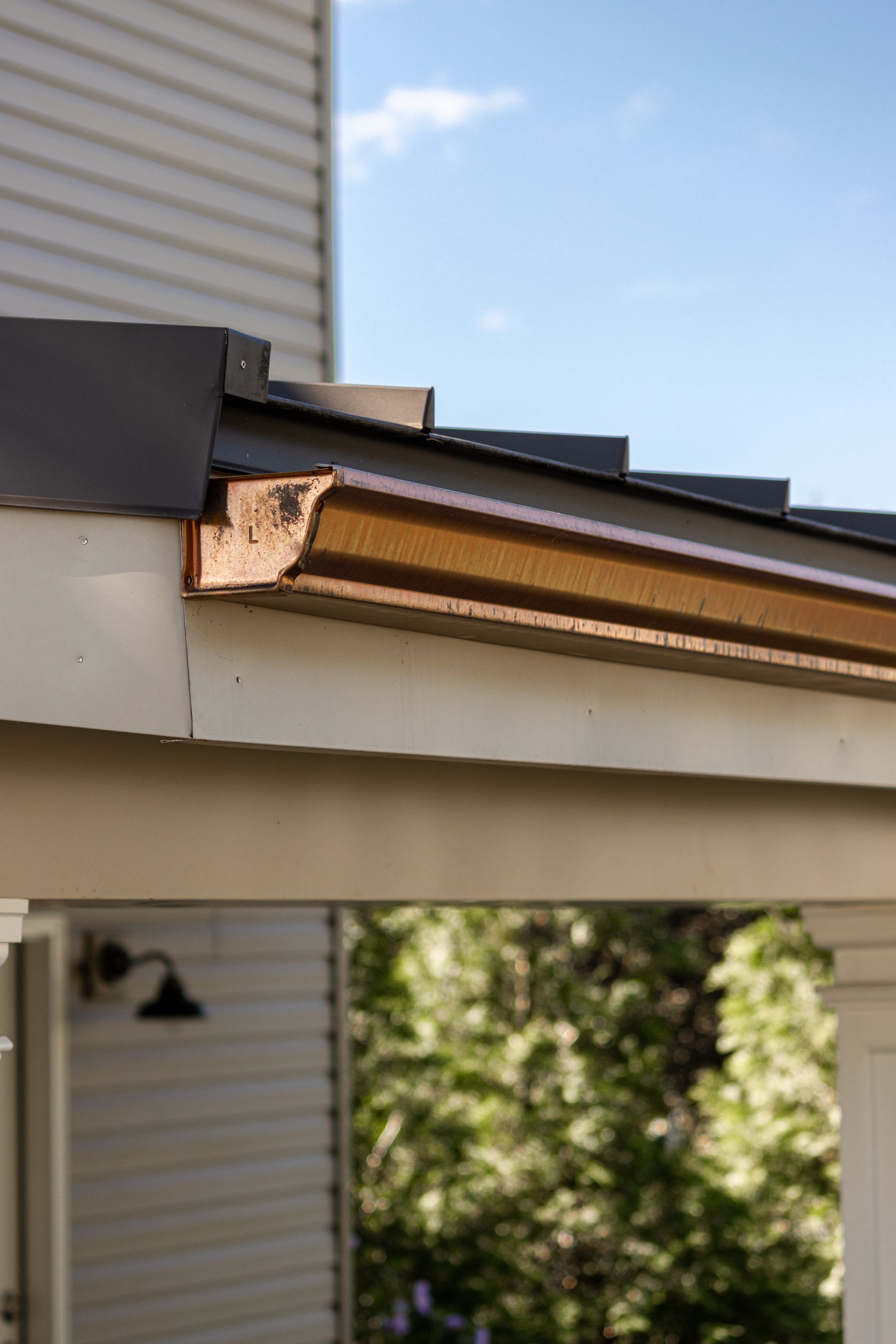 Damaged roof edge on a white building with brown trim, blue sky in background.