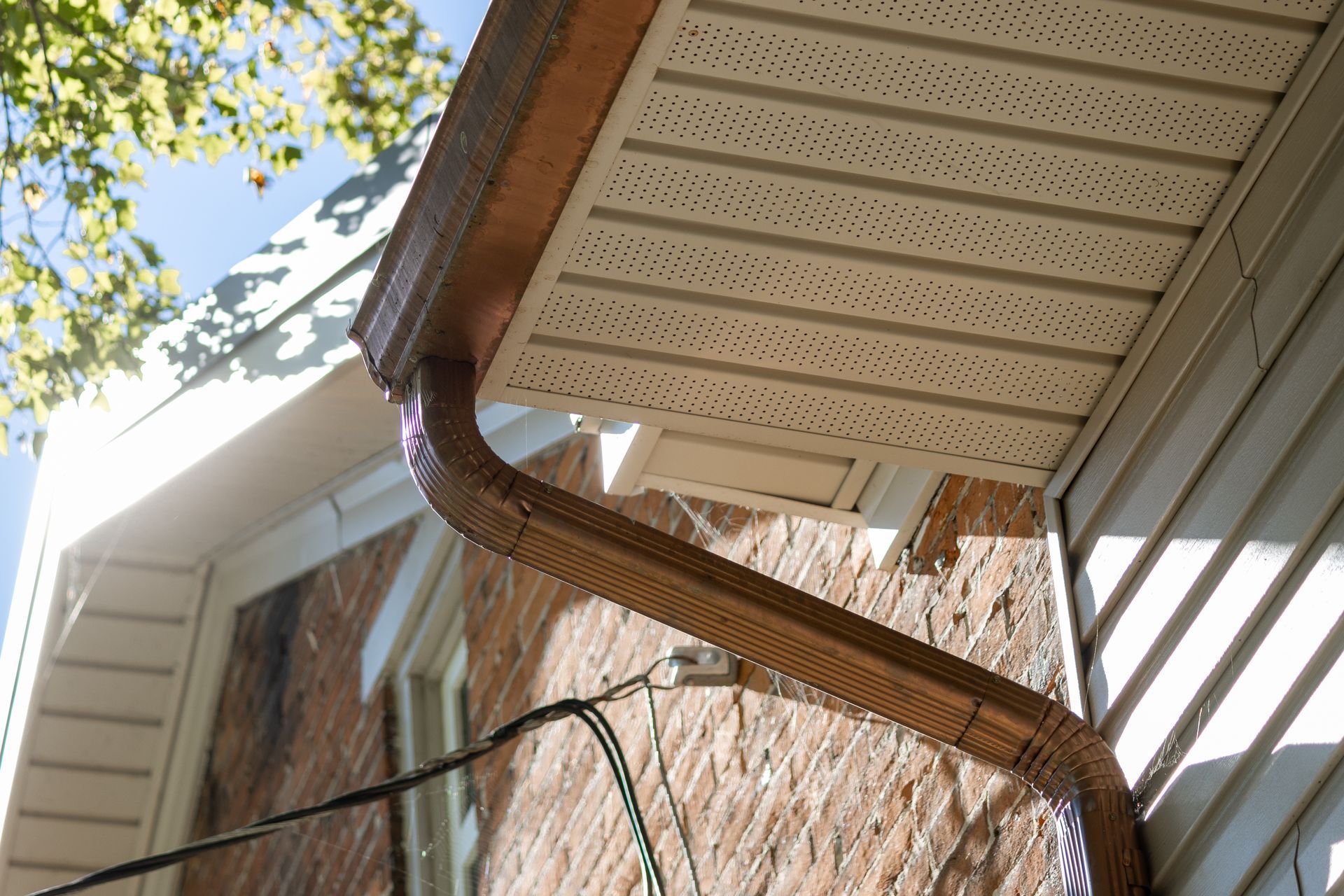 Brown gutters attached to a house with a brick and white siding.