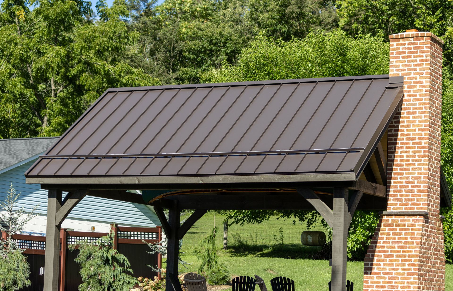 Brown metal roof on a wooden gazebo, with a brick chimney in a backyard setting.