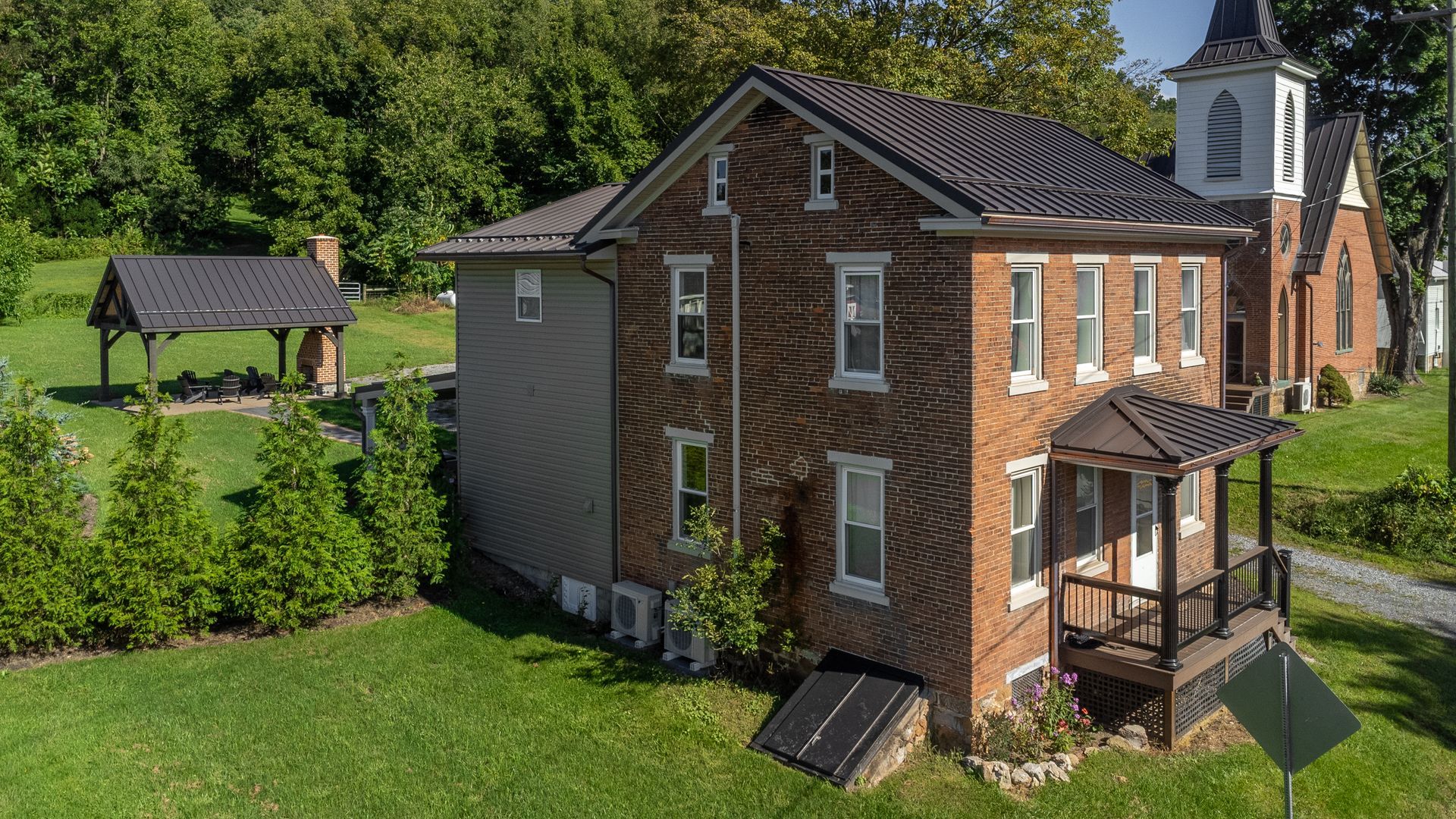 Brick building with a church steeple, a gazebo, and green grass under a sunny sky.
