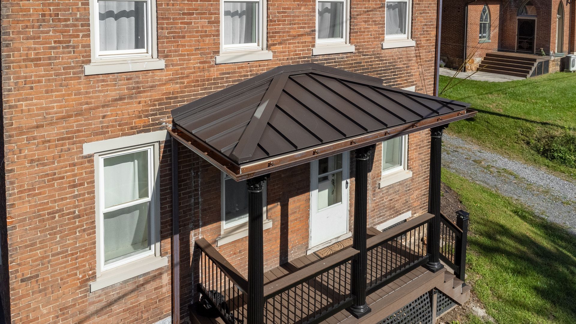 Brick building with a brown metal roofed porch, black posts, and railing.