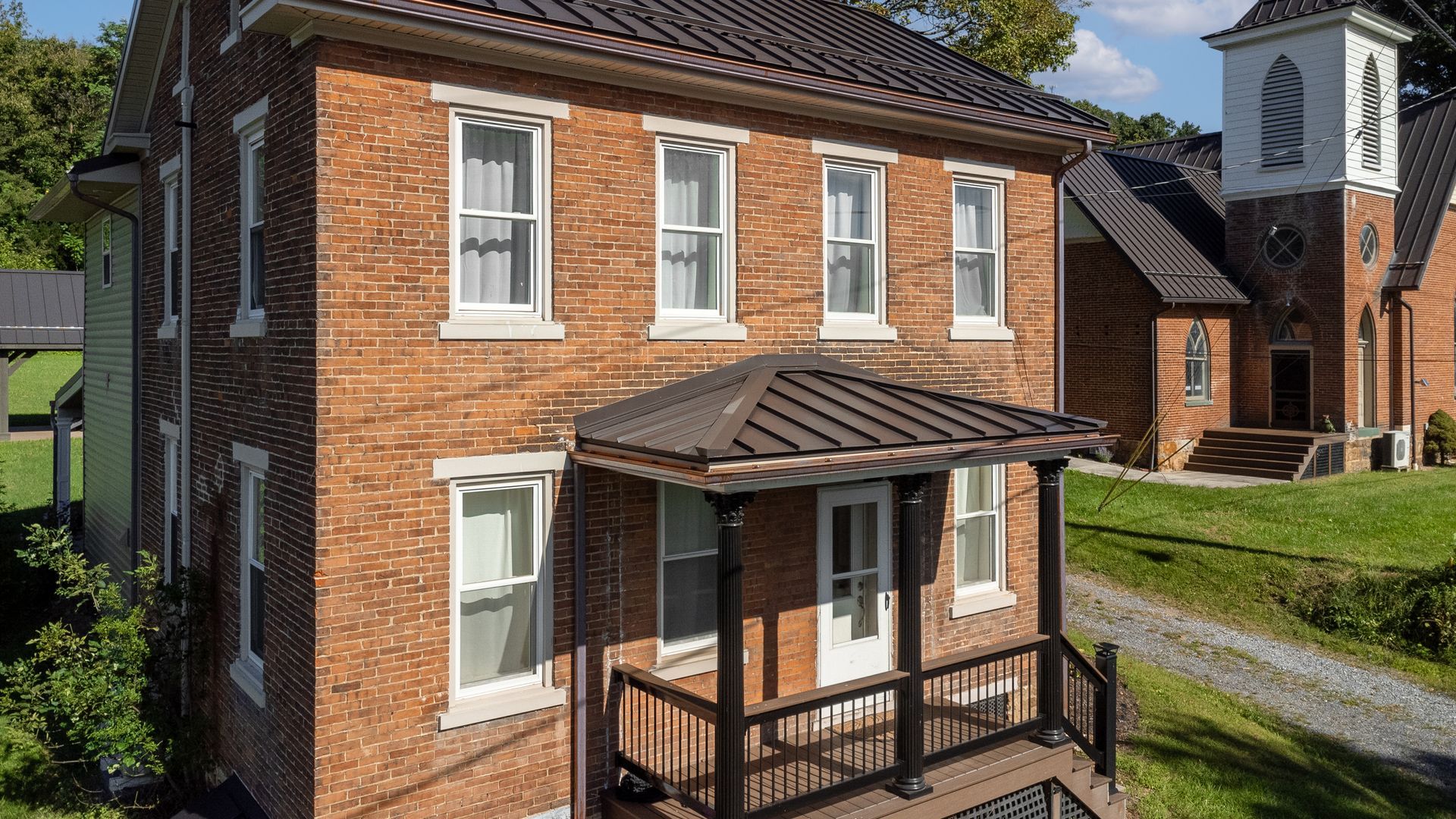 Red brick building with white-trimmed windows and a small porch, in front of a church.
